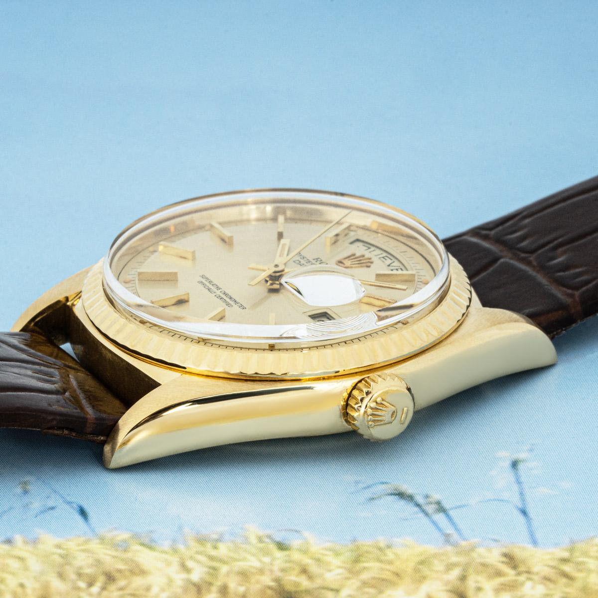 A 36mm Day-Date by Rolex in yellow gold. Featuring a champagne dial with applied hour markers and a fluted yellow gold bezel. Fitted with a plexiglass and a self-winding automatic movement. The watch is equipped with a generic brown leather strap