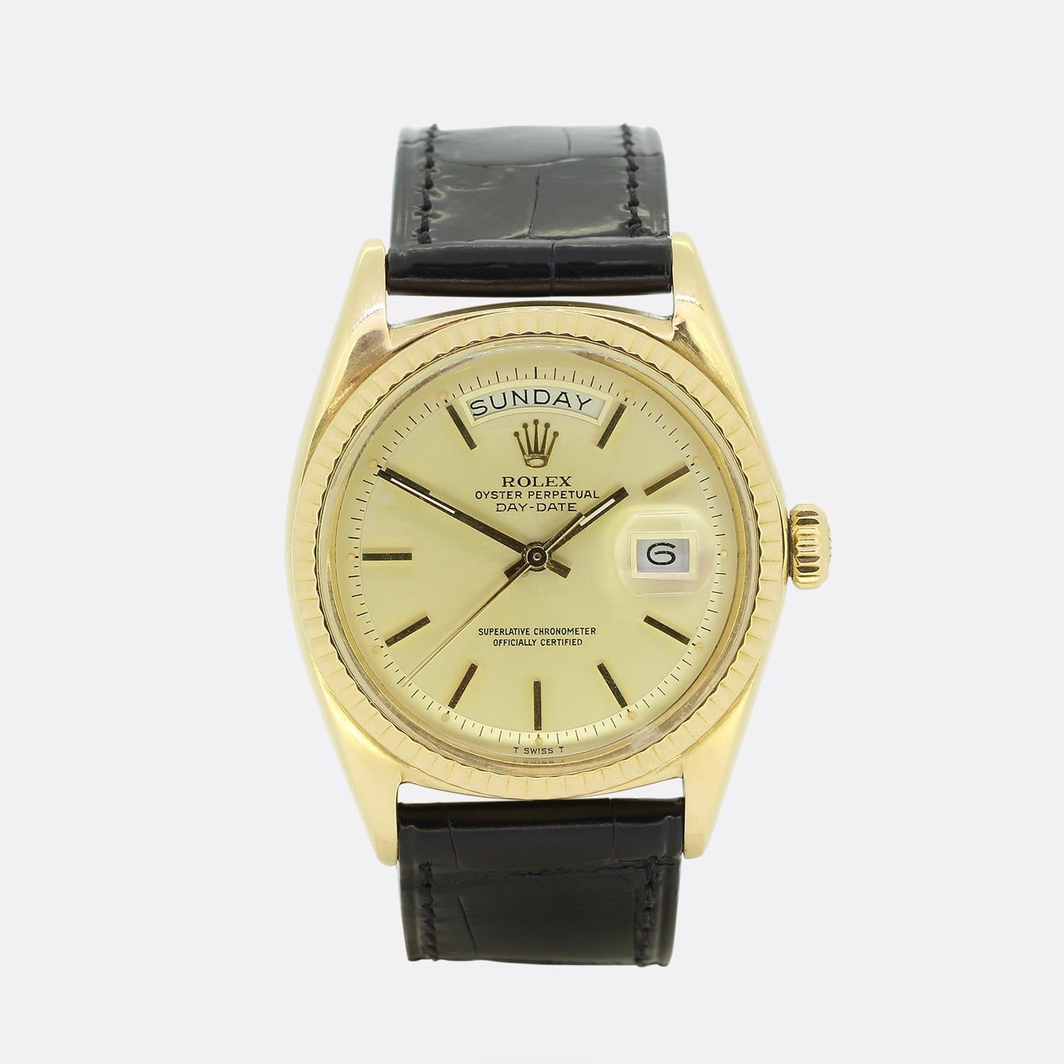This is a 1960s 18ct yellow gold Rolex Day-Date. The watch has a gold dial, gold hour hands, 3 o'clock date aperture, and is encased in an 18ct yellow gold casing with a fluted bezel. The watch has been finished with a black leather strap with black