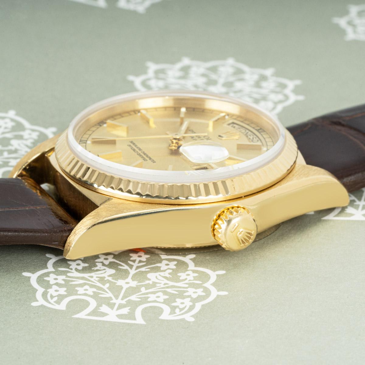 A yellow gold Day-Date by Rolex. Featuring a champagne dial with applied hour markers and a fluted yellow gold bezel. The watch is presented on a generic brown leather strap and equipped with a gold plated pin buckle. Fitted with a sapphire glass