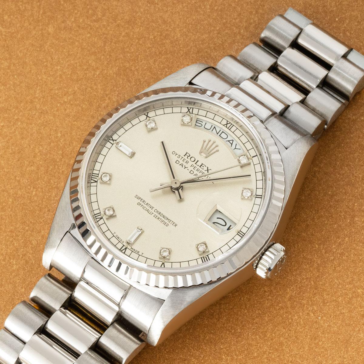 A 36mm Day-Date in white gold by Rolex. Features a silver dial set with 8 single cut diamonds, 2 baguette cut diamonds and a fixed white gold fluted bezel.

Fitted with sapphire crystal, a self-winding automatic movement and a president bracelet