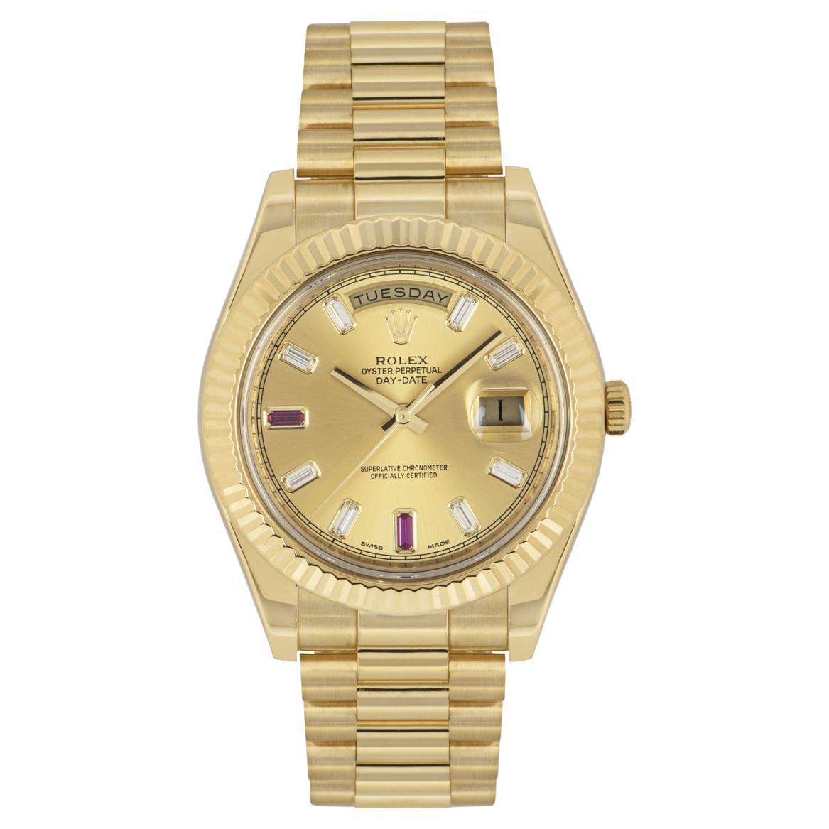 A yellow gold Day-Date II by Rolex. Features a champagne dial with 8 baguette cut diamonds and 2 baguette cut rubies. The fluted bezel, president bracelet and concealed folding Crownclasp are signature Day-Date characteristics. Fitted with scratch