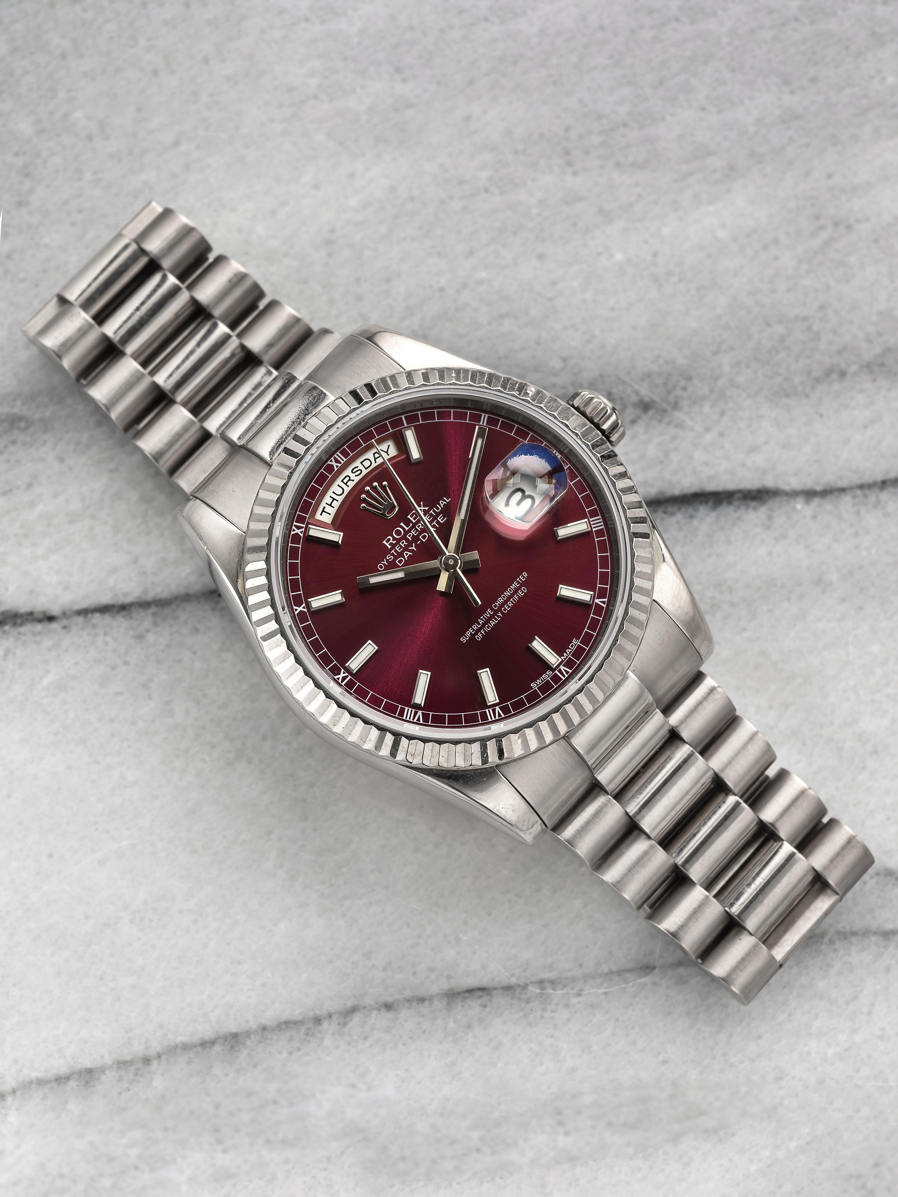 Here's a Rolex Day-Date reference 118239 automatic with a cherry red dial in 18k whtie gold from the 2000s. Quickset day and date function at 3 and 12 a clock. Measurements include a 36mm case, 20mm lug width, and a bracelet that fits up to a 6.75