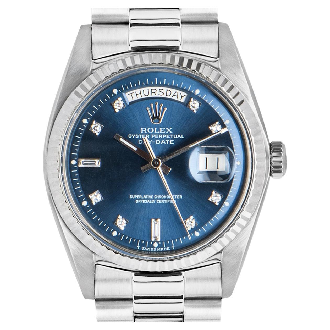 An 18k white gold Day-Date men's wristwatch, by Rolex.

The iconic day and date apertures are showcased on a blue dial, which is set with a mix of round brilliant cut and baguette cut diamond hour markers. Complementing the dial is a plastic glass
