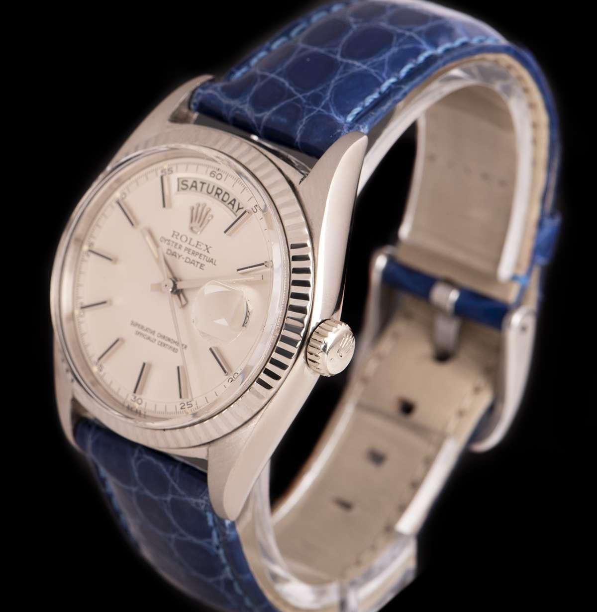 An 18k White Gold Oyster Perpetual Day-Date Vintage Gents Wristwatch from 1964, silver dial with applied hour markers, day aperture at 12 0'clock, date aperture at 3 0'clock, a fixed 18k white gold fluted bezel, a blue leather strap with a stainless