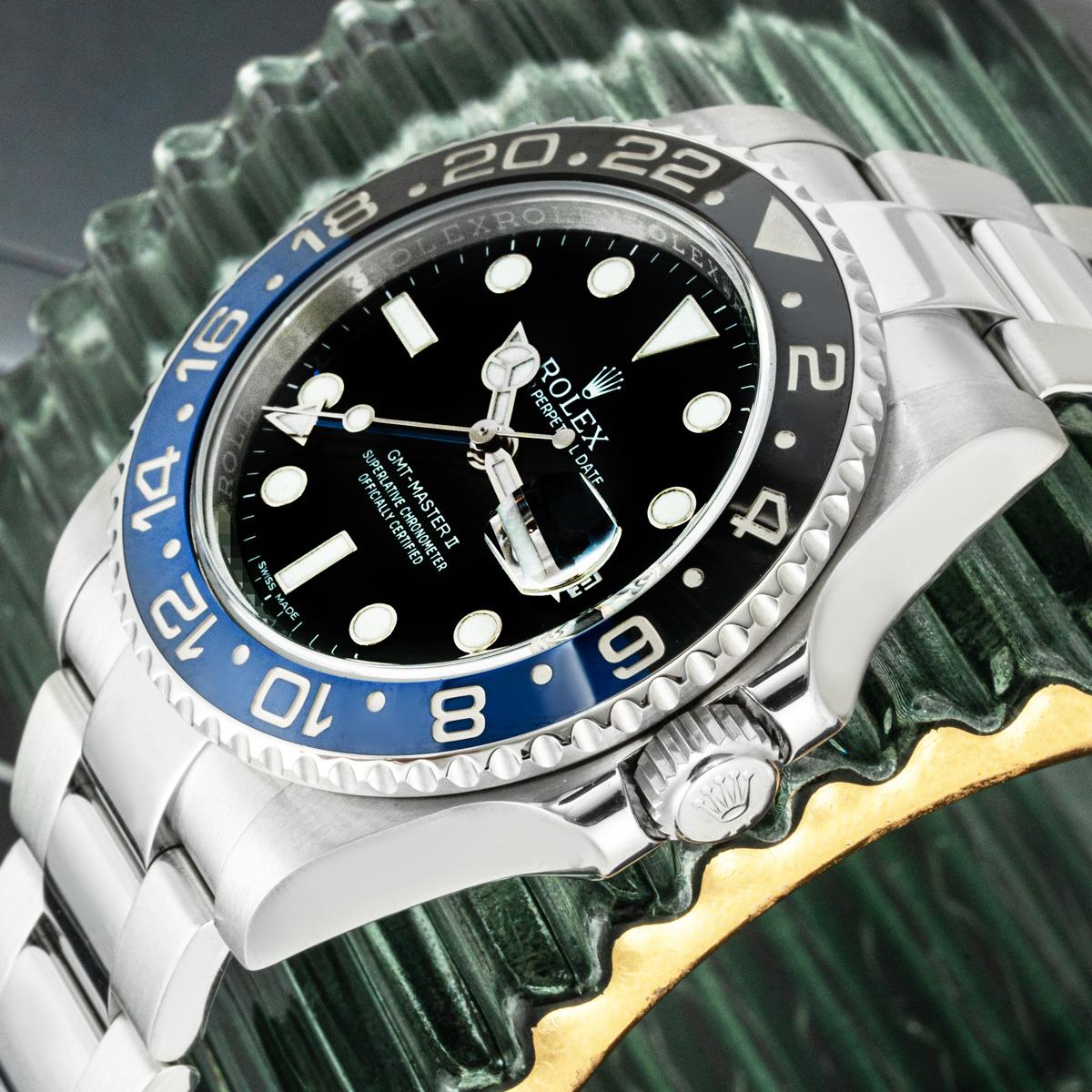 An Oystersteel GMT-Master II Batman by Rolex, featuring a black dial with the date and blue time zone hand. The ceramic black and blue bidirectional rotatable bezel features a 24-hour display. The Oyster bracelet comes equipped with a folding