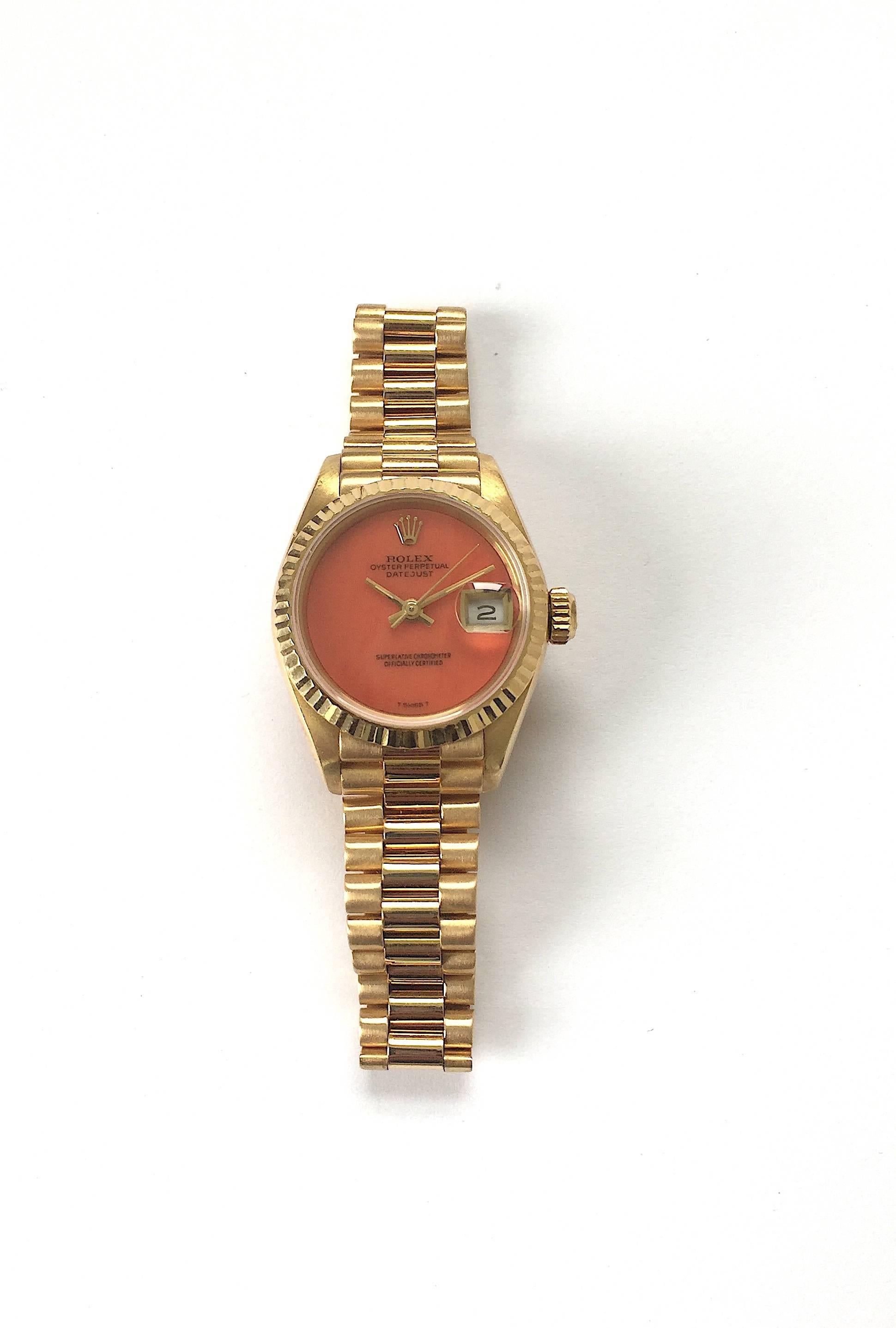 Rolex 18K Yellow Gold Ladies Datejust Watch 
Rare Factory Coral Dial with Applied Rolex Logo
Yellow Gold Gold Fluted Bezel
18K Yellow Gold Case
26mm in size 
Features Rolex Automatic Movement with Quick-Set Date Function
Acrylic Crystal
From Late