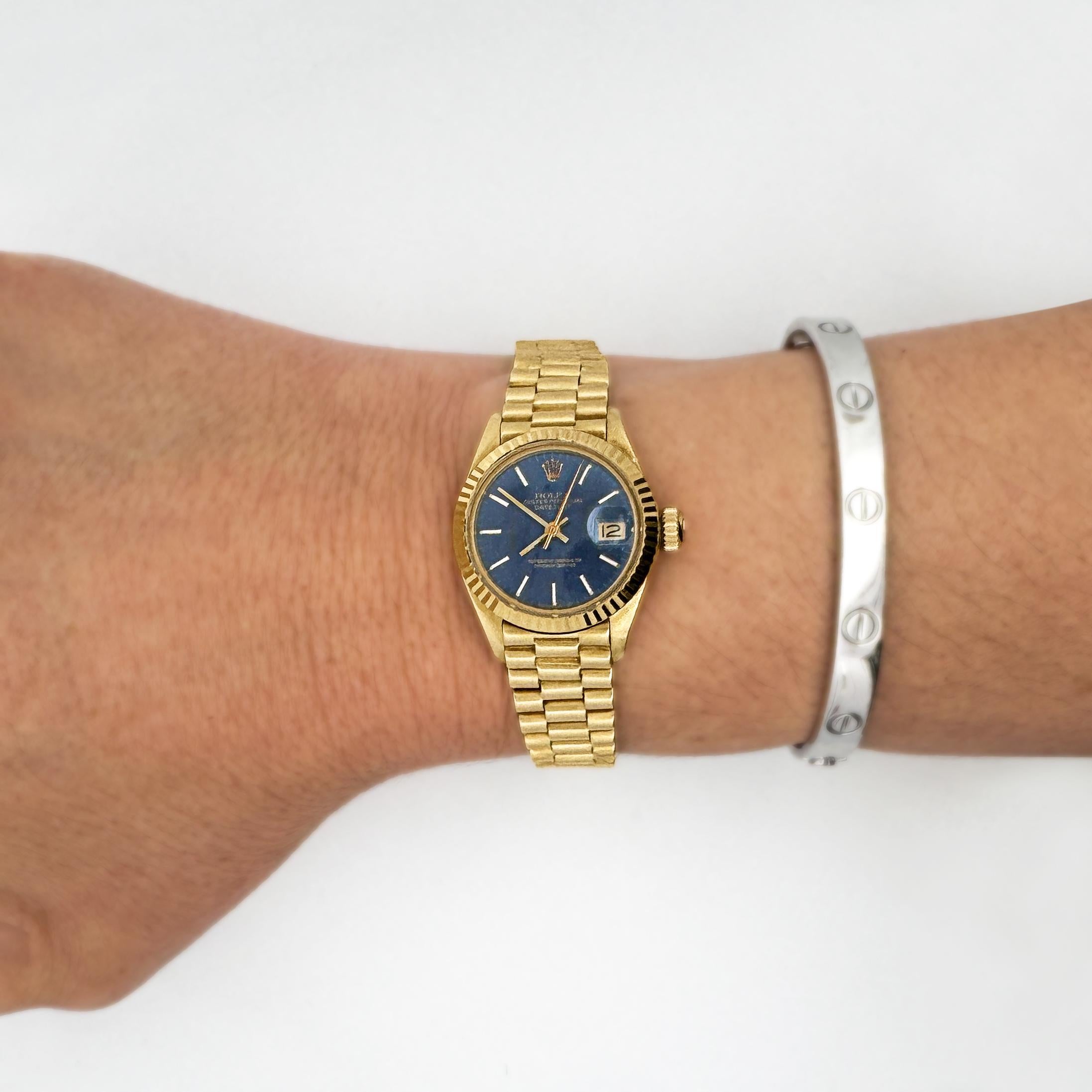 Rolex Lady DateJust 6917 en or 18 carats avec mouvement automatique, cadran bleu et bracelet président. Complet avec sa boîte et ses papiers.

Vendue avec la boîte de service d'origine de Rolex, le certificat d'origine, le reçu, le maillon