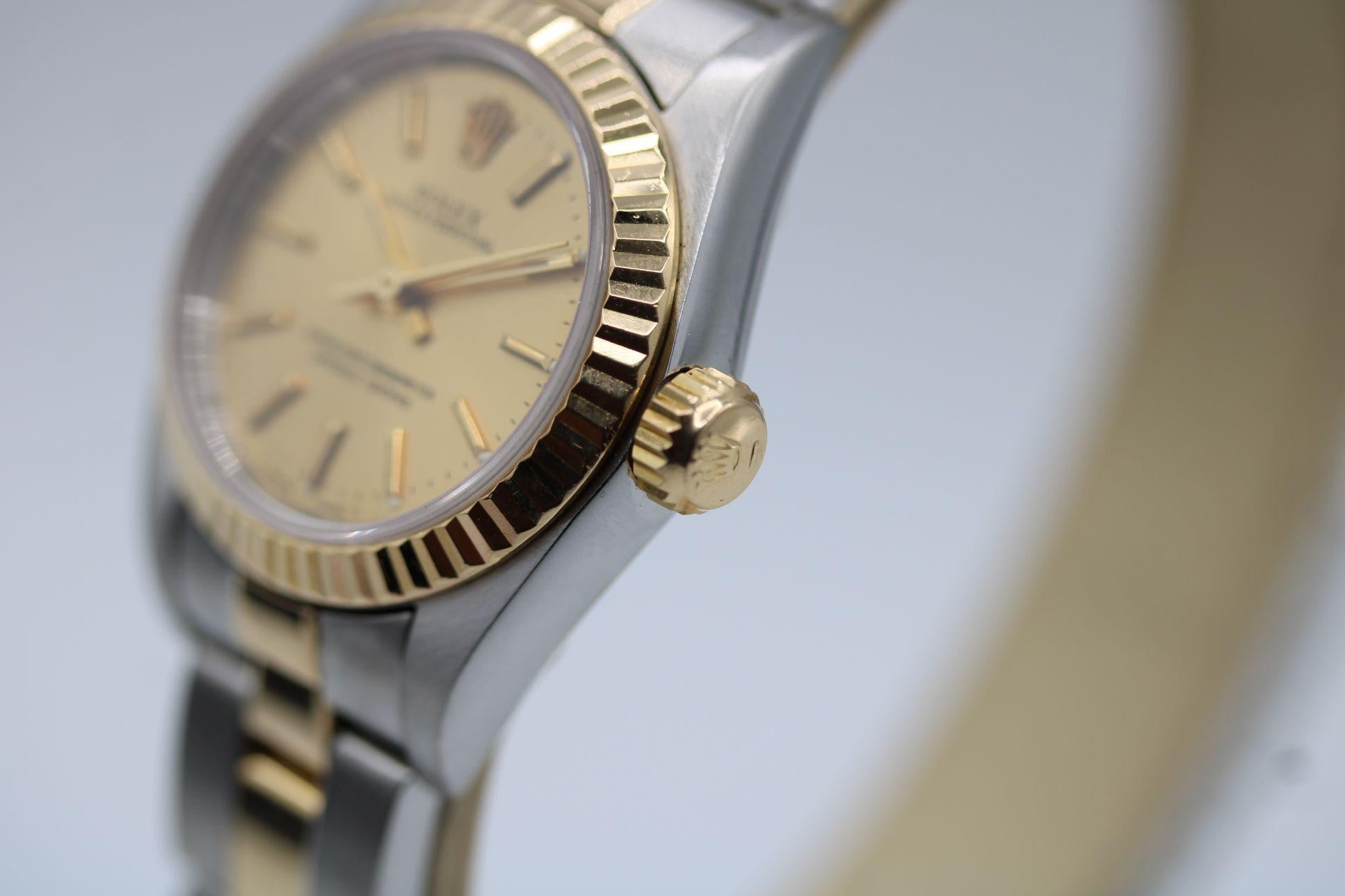 Diese Rolex Oyster Perpetual Lady, Modell 67193, verfügt über ein 26-mm-Edelstahlgehäuse, eine kannelierte Lünette aus Gelbgold, ein goldenes Zifferblatt mit Stabindexen und passenden Zeigern sowie ein Saphirkristallglas.

Die Uhr wird von einem