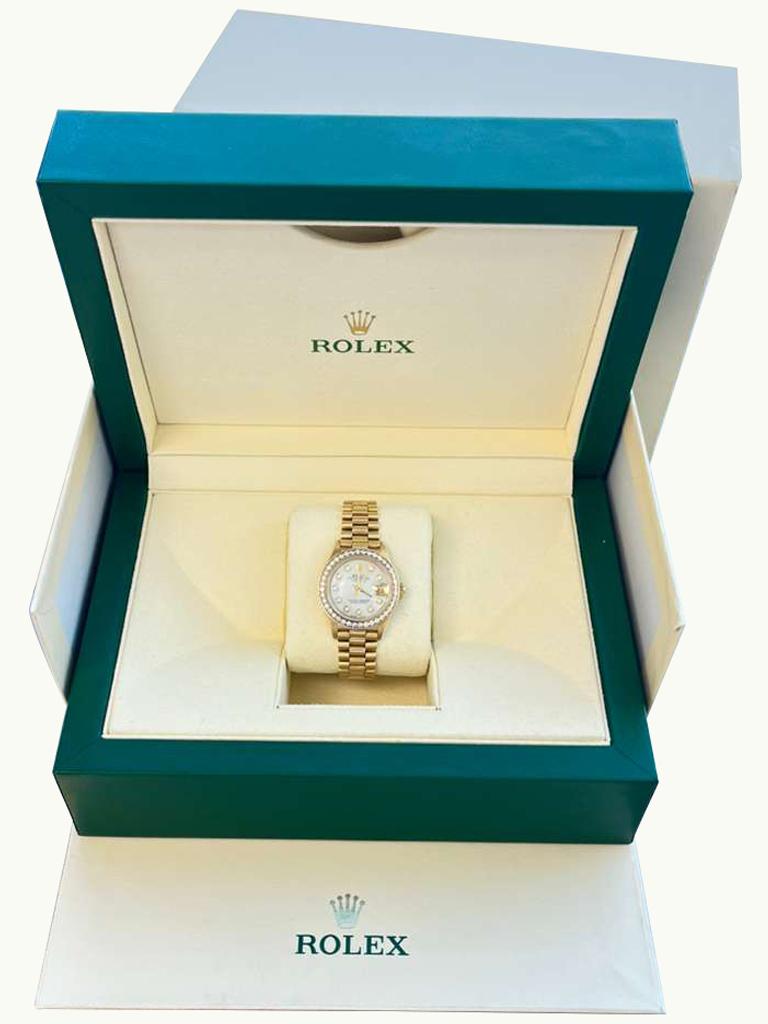 Cette exquise Rolex Lady-Datejust President en or jaune 18 carats massif est un modèle de luxe et d'élégance féminine. D'une taille de 26 mm, elle est dotée d'une lunette en diamant Aftermarket magnifiquement travaillée qui capte la lumière et