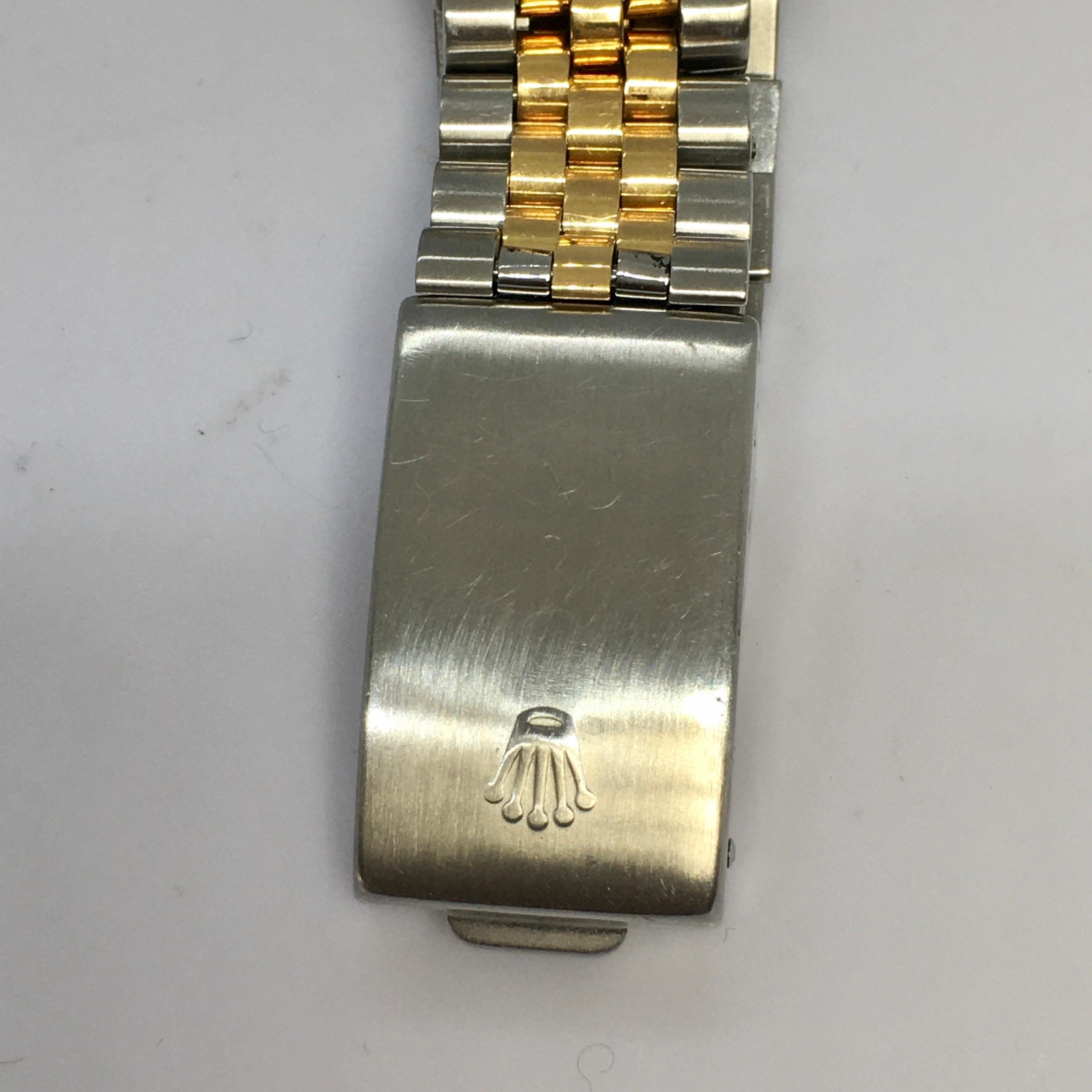 This Rolex men's wristwatch is a luxury timepiece with a round silver case and a blue and gold bezel. The watch features baton indexes on a gold dial, with a quickset function and a 12-hour analog display. The watch is made of stainless steel and