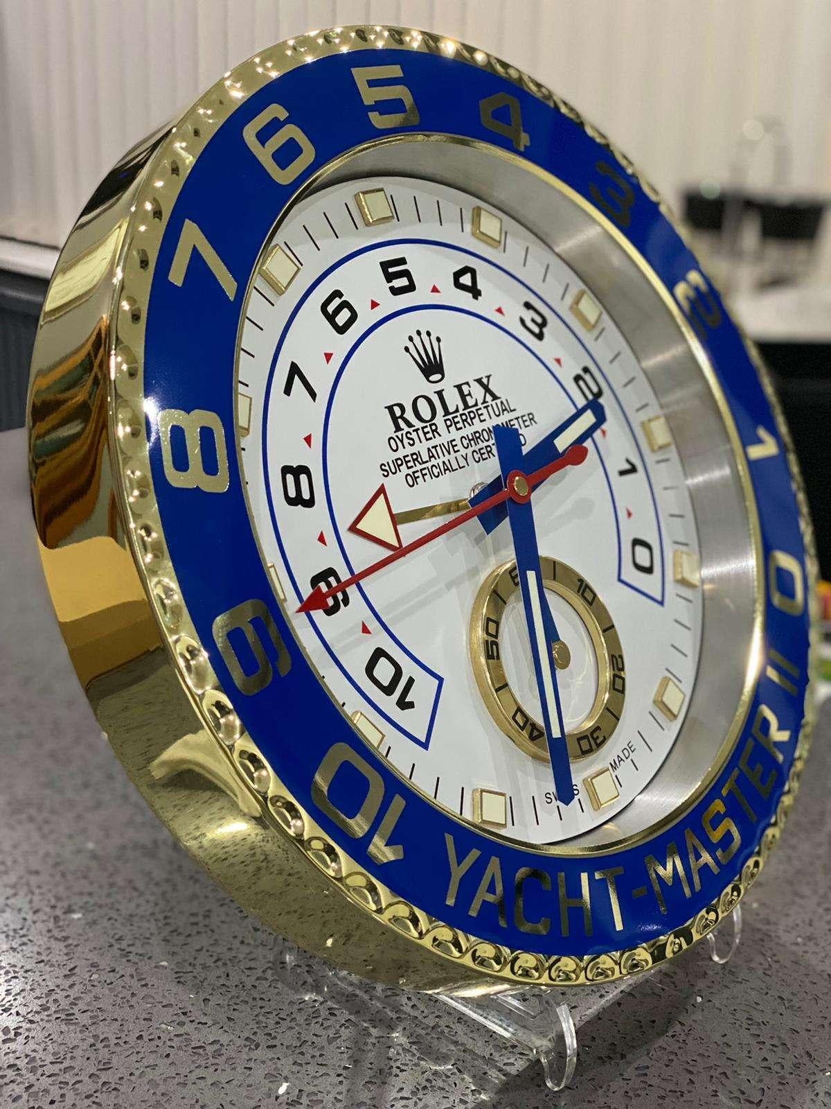 ROLEX Officially Certified Chrome Gold and Blue Yacht Master II Wall Clock
Good condition, working.
Lume strips Sweeping Quartz movement powered by single AA Battery.
Clock dimensions measure approximately 35cm by 5cm thickness

These wall clocks