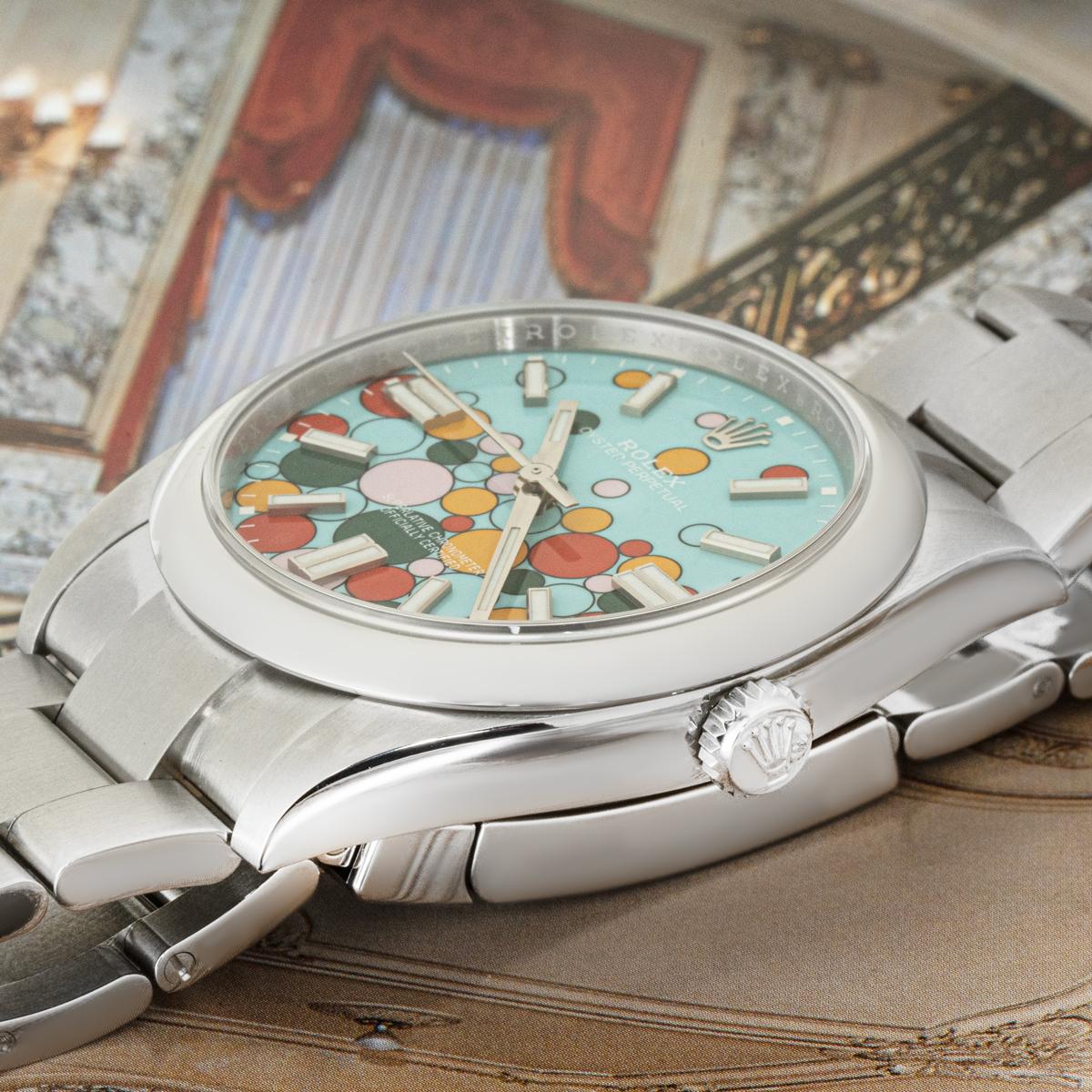 A 41mm Oyster Perpetual from Rolex in Oystersteel. Featuring the Celebration motif dial which has various-sized bubbles in candy pink, yellow, coral red and green against a turquoise blue background which is a reminder of the coloured dials