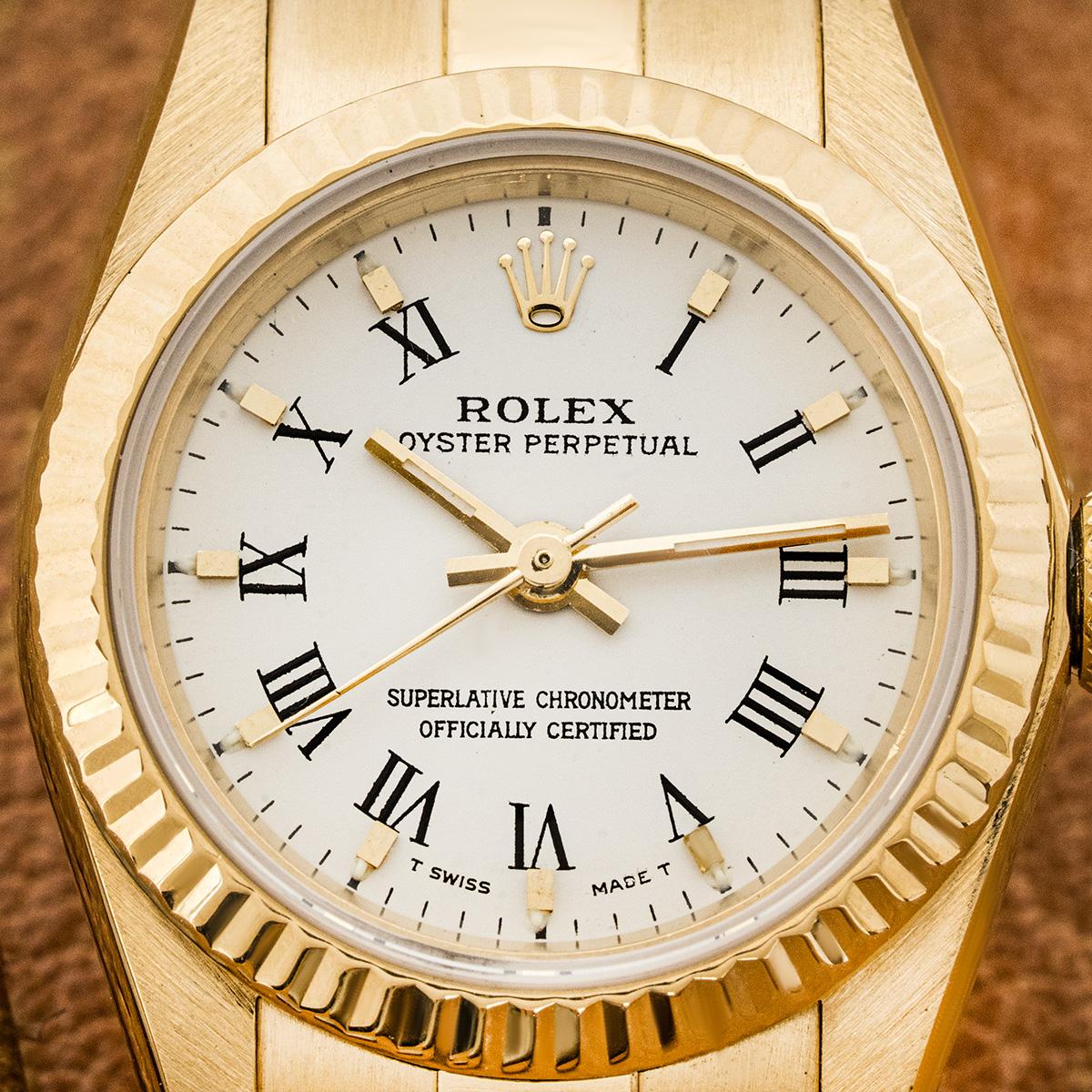A ladies 24mm Oyster Perpetual in 18k yellow gold by Rolex. Featuring a white dial with roman numerals and a yellow gold fluted bezel. The watch is fitted with a sapphire crystal, a self-winding automatic movement and equipped with a yellow gold