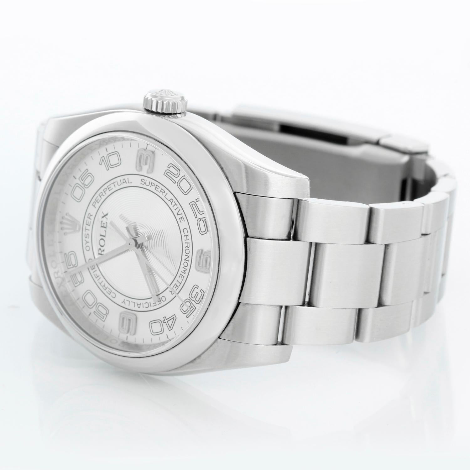 Montre Rolex Oyster Perpetual pour homme en acier inoxydable 116000 - Remontage automatique, 31 rubis, verre saphir. Boîtier en acier inoxydable avec lunette lisse (36 mm de diamètre). Cercles concentriques noirs avec chiffres arabes blancs .