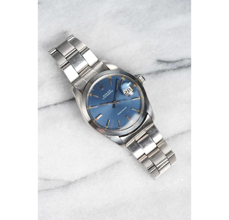 Aquí tienes una Rolex Oysterdate vintage de precisión con número de referencia 6694 de cuerda manual y esfera azul soleada de finales de los 60, principios de los 70. Mantiene la hora y es totalmente funcional. Las medidas incluyen una caja de ostra