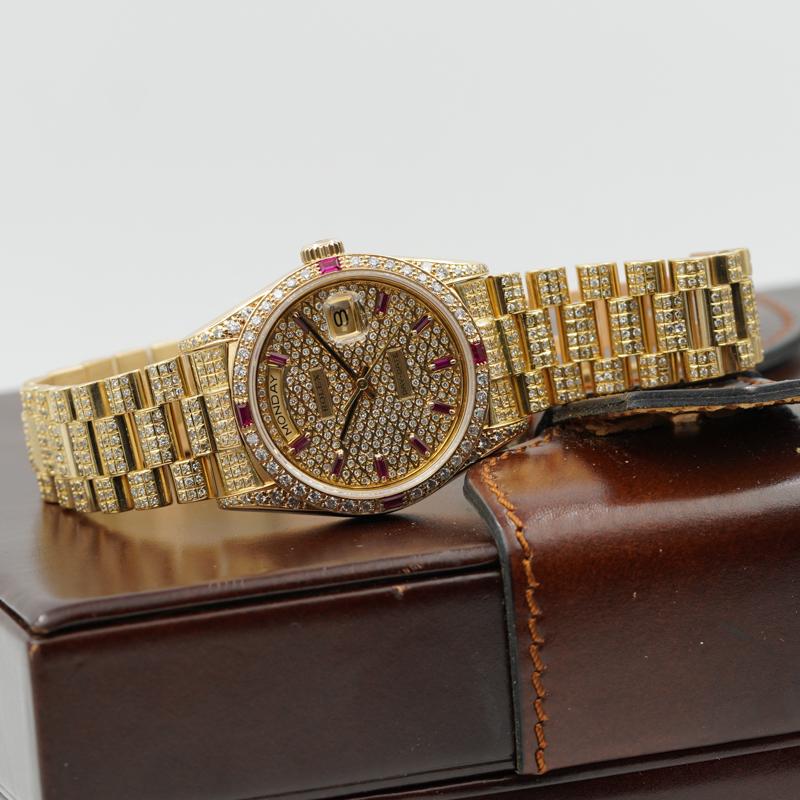 This modified Rolex President with custom diamonds and rubies was recently traded in to our store and is in very good condition. The watch's bracelet and case are made of 18K yellow gold. The watch dial, bezel, and bracelet all have  diamonds and