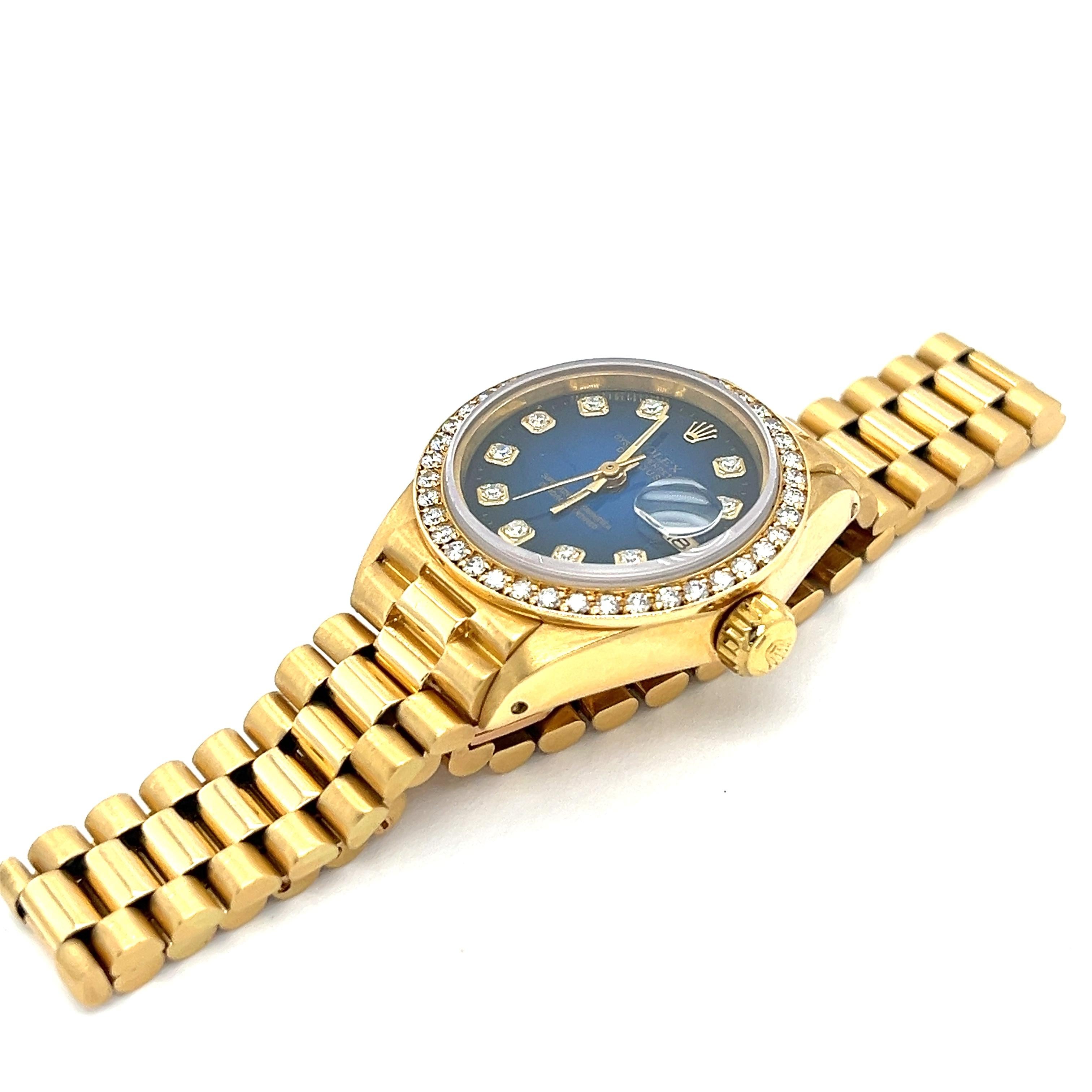 Women's Pre-owned 26mm Rolex Datejust President in 18K yellow gold. Embellished with 10 round diamond dial markers and a captivating blue dial, this Datejust President watch is a keepsake to last generations. Complete with a bead set bezel  and hour
