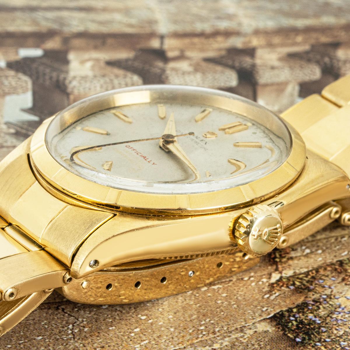 A rare Oyster Perpetual wristwatch in yellow gold by Rolex. Featuring a silver dial with a distinctive 'Officially' in red writing and a yellow gold engine turned bezel. Fitted with a plastic glass and a self-winding automatic movement. The watch is