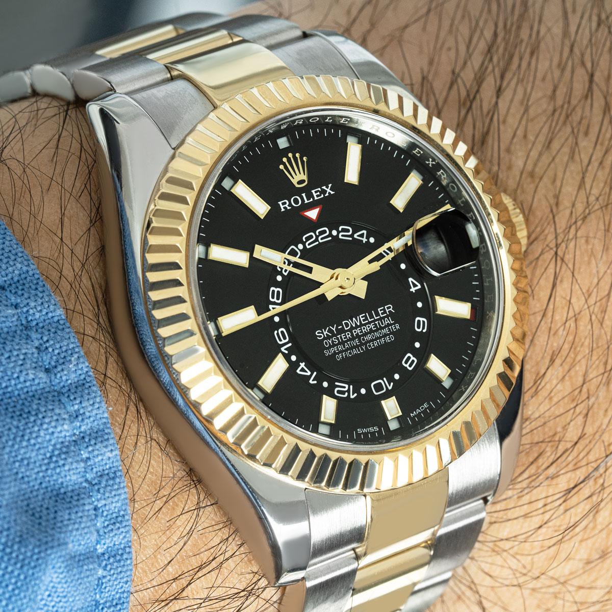 A Sky-Dweller in Oystersteel and yellow gold by Rolex. Featuring a black dial with the date indicator, a month display via the 12 apertures, a 24 hour display, and a second time zone which can be set using the fluted yellow gold bidirectional