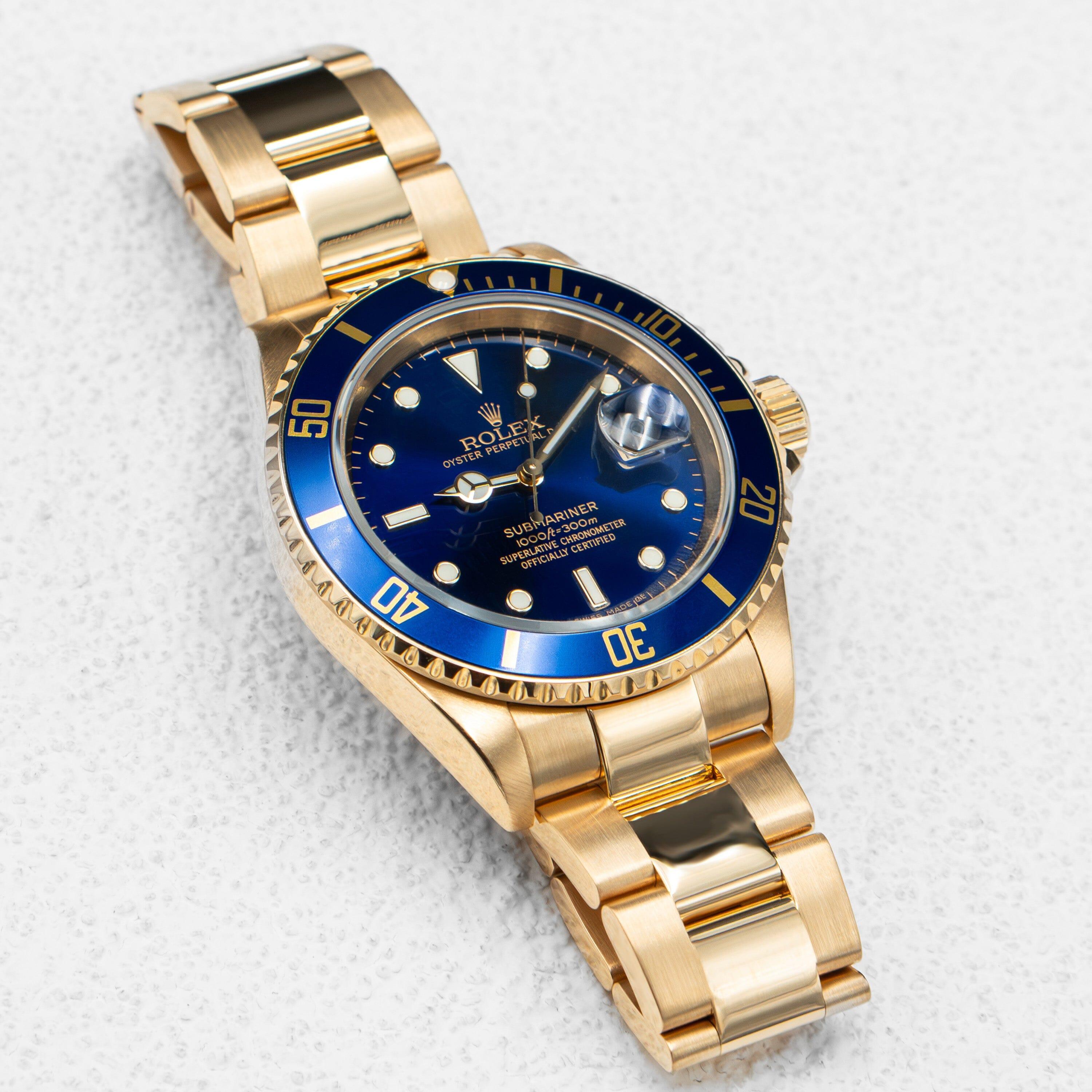 Rolex Submariner 16618 Herrenuhr. 40mm 18K Gelbgold Gehäuse. Einseitig drehbare Lünette aus 18 Karat Gelbgold mit blauem Einsatz. Blaues Zifferblatt mit goldfarbenen Leuchtzeigern und Leuchtpunktindexen. Datumsanzeige auf der 3-Uhr-Position. 18K