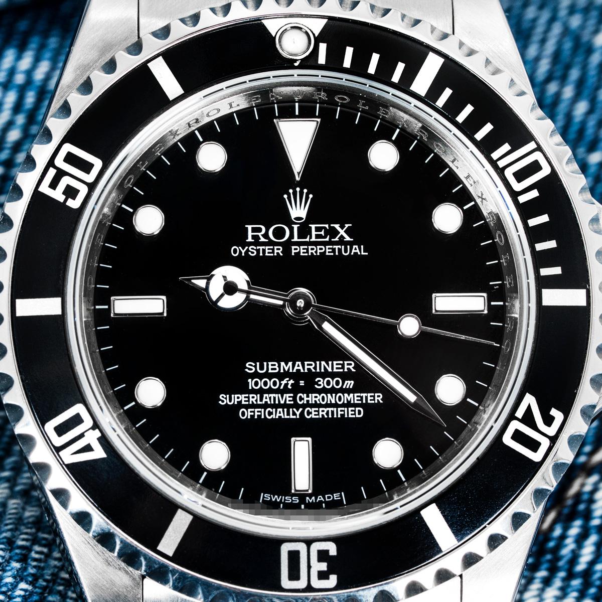 Eine Oystersteel Submariner Non-Date von Rolex. Sie verfügt über ein schwarzes Zifferblatt mit einem markanten 4-Linien-Schriftzug und eine unidirektional drehbare Lünette mit schwarzem Lünetteneinsatz und 60-Minuten-Teilung. Das Oyster-Armband wird