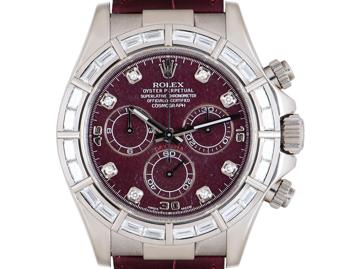 A 40 mm unworn NOS Daytona from Rolex in white gold that features a rare rubellite dial set with 8 round brilliant cut diamond hour markers. Featuring 24 baguette cut diamonds on the bezel. The original maroon leather strap comes with an Oysterlock