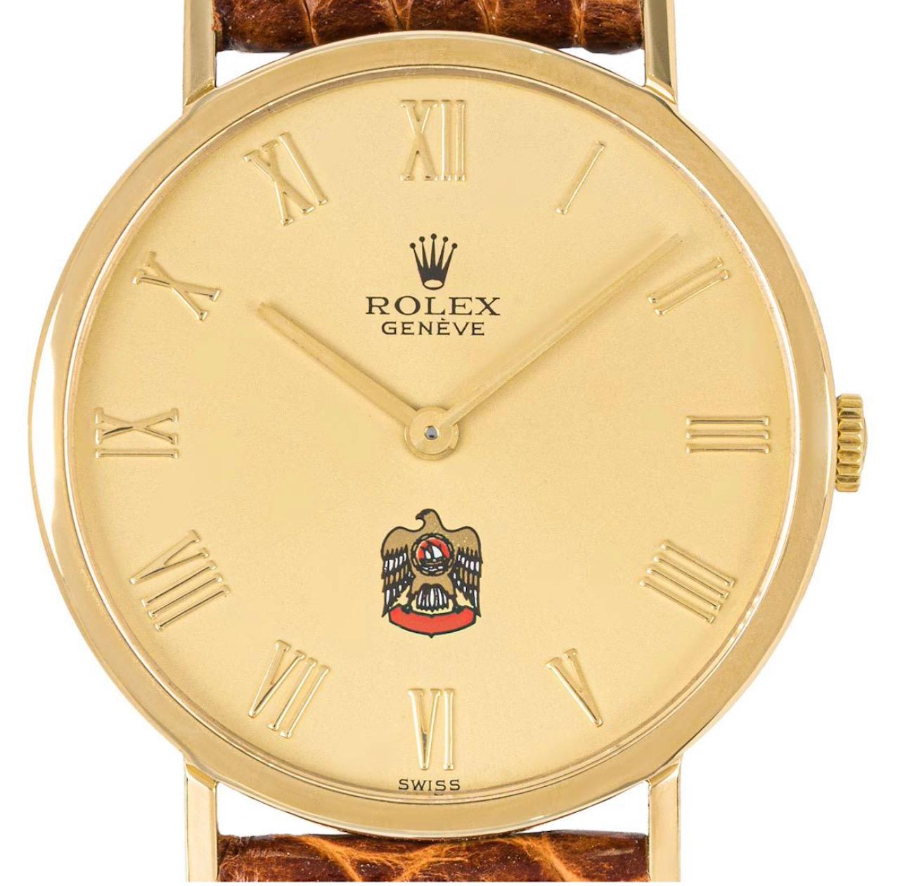 Une montre-bracelet Cellini de 32 mm en or jaune par Rolex. Il présente un cadran argenté avec un emblème distinctif des Émirats arabes unis à 6 heures et des chiffres romains appliqués. Dotée d'un verre saphir, d'un mouvement à remontage manuel et