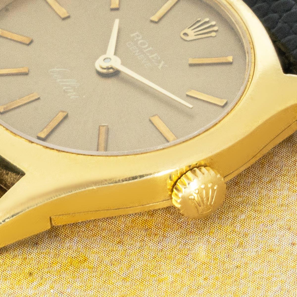 A vintage Cellini wristwatch in yellow gold by Rolex. Features a champagne dial with applied hour markers. Fitted with sapphire glass and a manual wind movement, the piece is presented on a generic black leather strap (navy blue alternative shown in