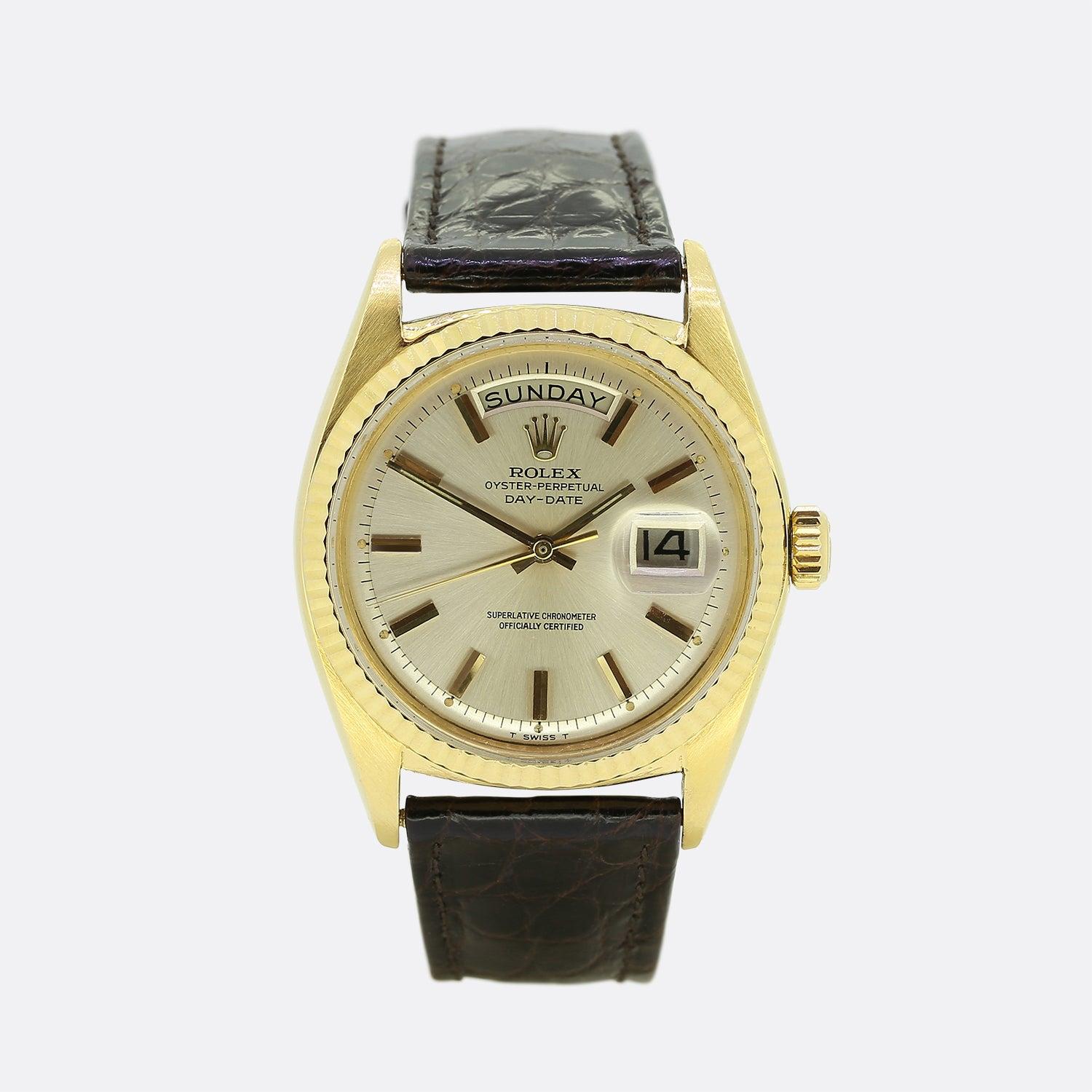 This is a vintage, 18ct yellow gold Rolex Day-Date. The watch has a silver dial, gold hour hands, 3 o'clock date aperture, and is encased in an 18ct yellow gold casing with a fluted bezel. The watch has been finished with a Rolex dark brown leather