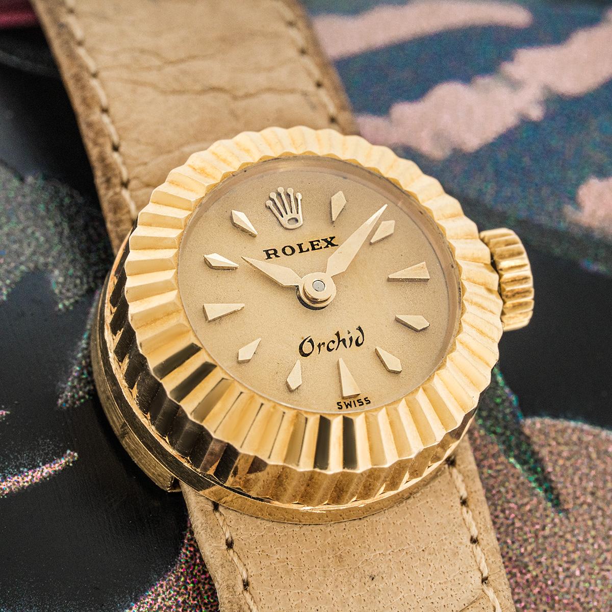 A vintage ladies Orchid Chameleon wristwatch in yellow gold by Rolex. Features a champagne dial with applied hour markers and a yellow gold fluted bezel.

Fitted with a plastic glass, a manual winding movement and an original brown leather strap