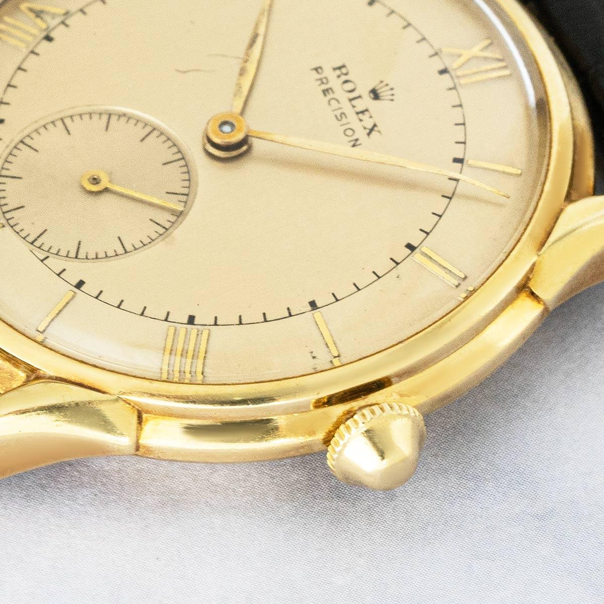 A 33mm vintage Rolex Precision in yellow gold. Features a champagne dial with Roman numerals and small seconds display. The piece is fitted with plastic glass, a manual wind movement, and a generic black leather strap which comes with a generic gold