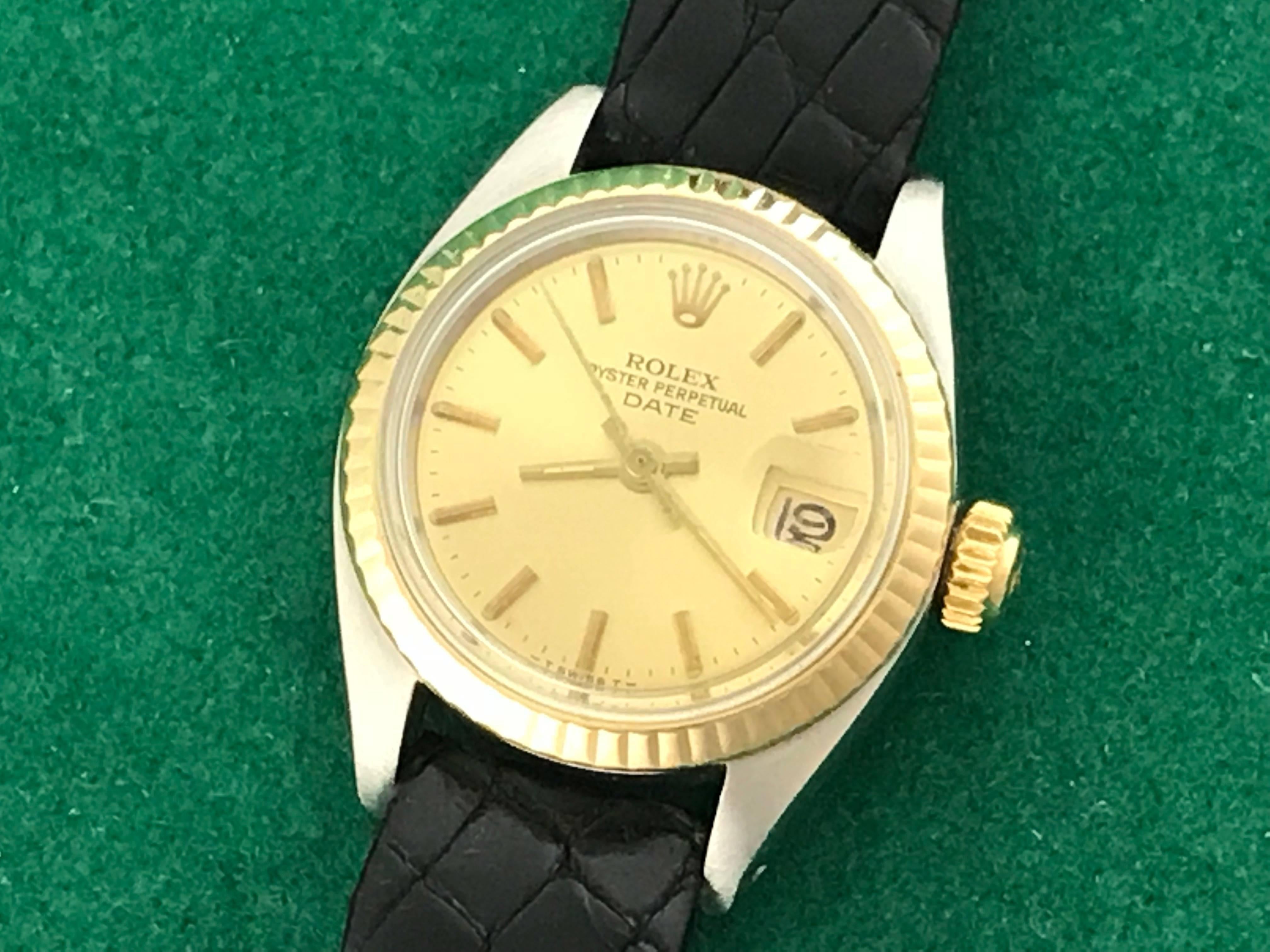 The Rolex Date Model 6917 Ladies automatic wrist watch. Featuring a champagne dial with yellow gold hour markers and stainless steel case with 14k yellow gold fluted bezel. Measures 25mm. Comes with a black alligator strap, box, instruction booklet