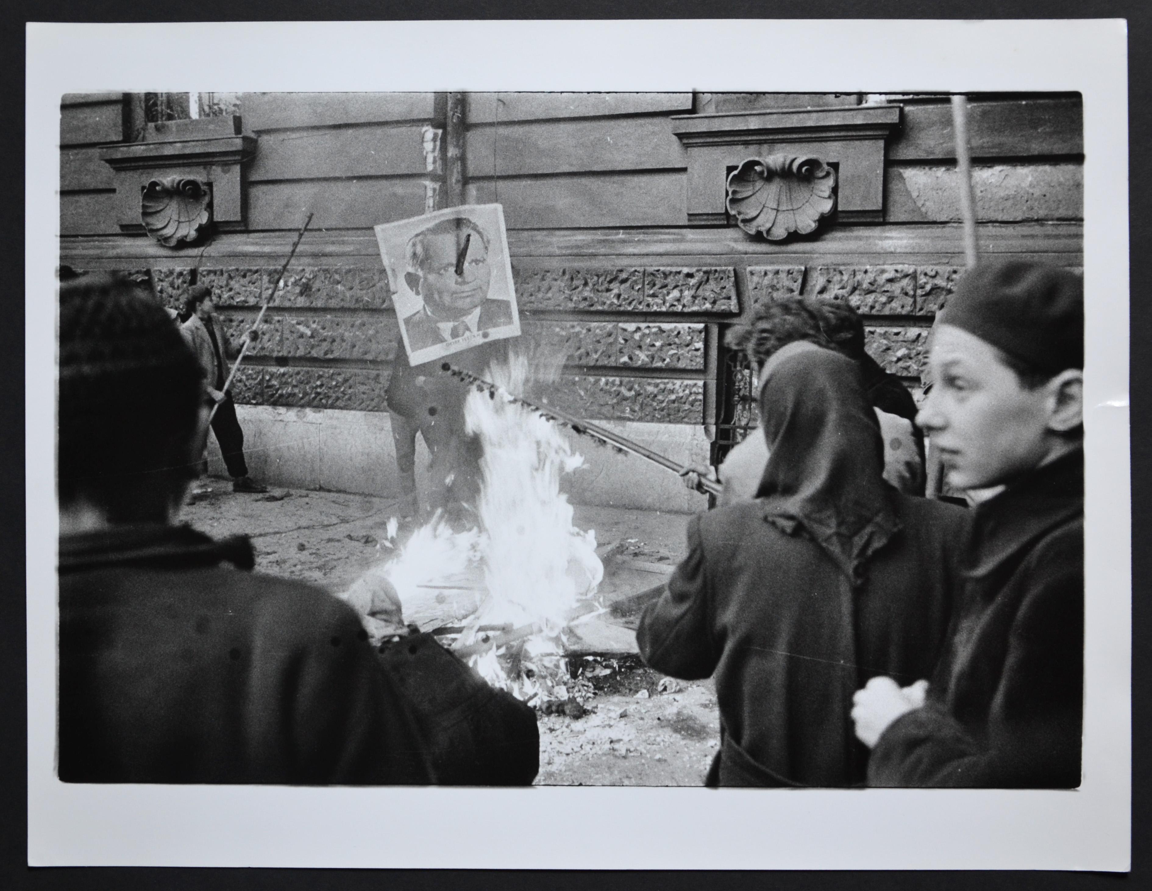 Rolf Gillhausen Black and White Photograph - Hungary uprising in back a fire with a poster of Istvan Dobi, 1956.