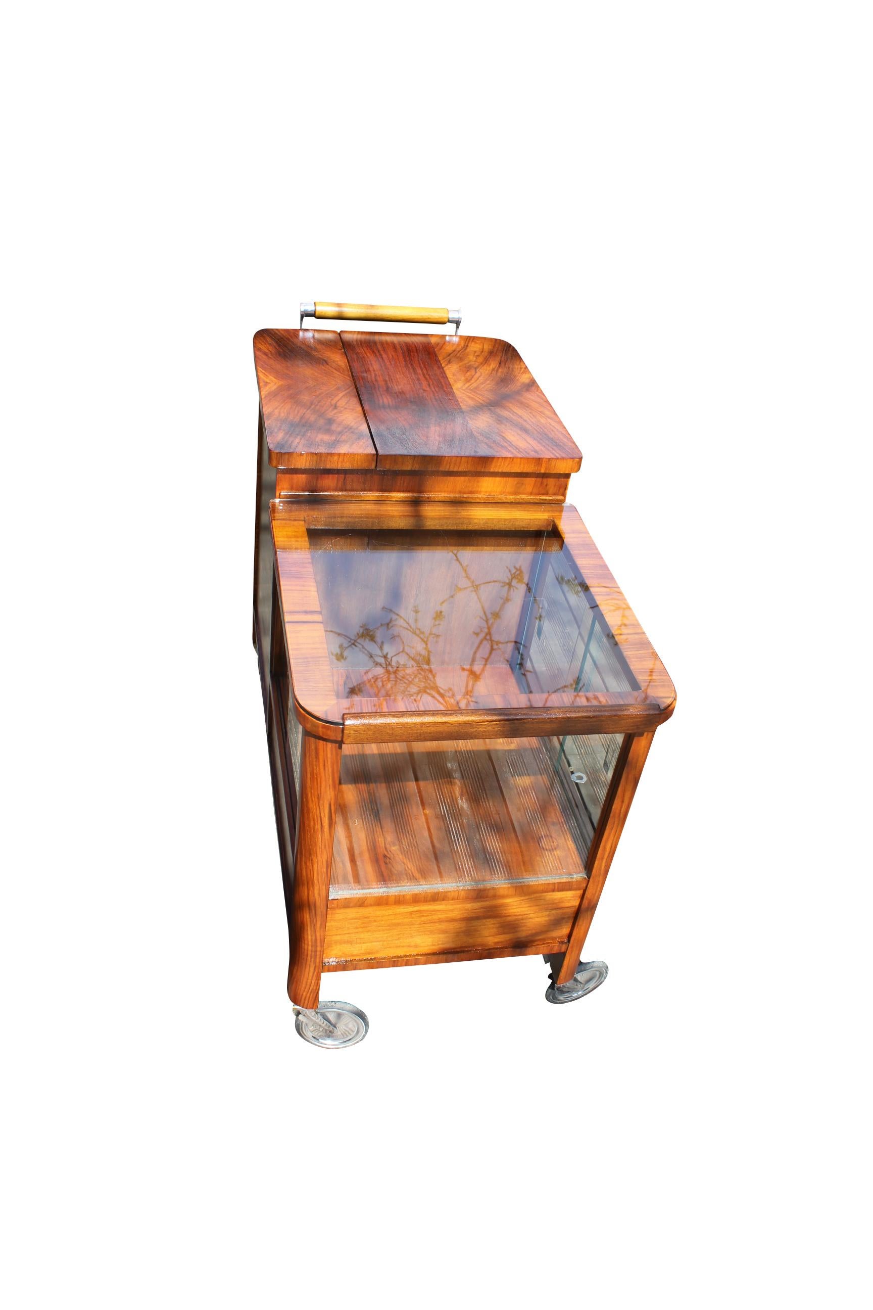 An Art Deco bar on wheels. The piece of furniture consists of a showcase, perfect for exhibiting your belongings, a lockable drawer and a hinged compartment for cooling the drinks. The wood has been polished by hand to high gloss and shines in a