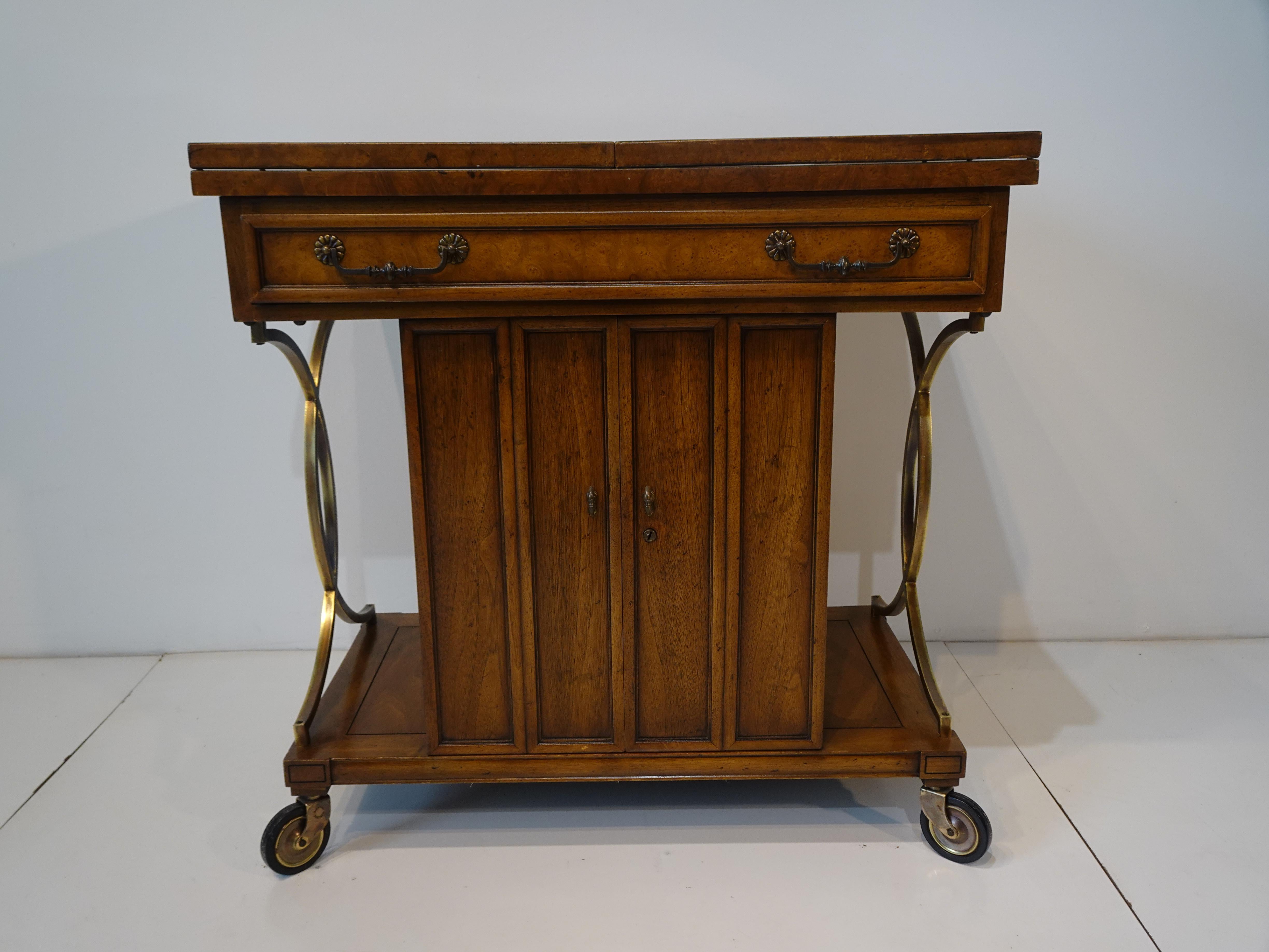 A very well constructed mahogany and burl wood rolling bar cart with expanding flip top having a satin black laminate surface and pull out stretchers for support. Below the top is a lower long center drawer with double doors a shelve, storage and