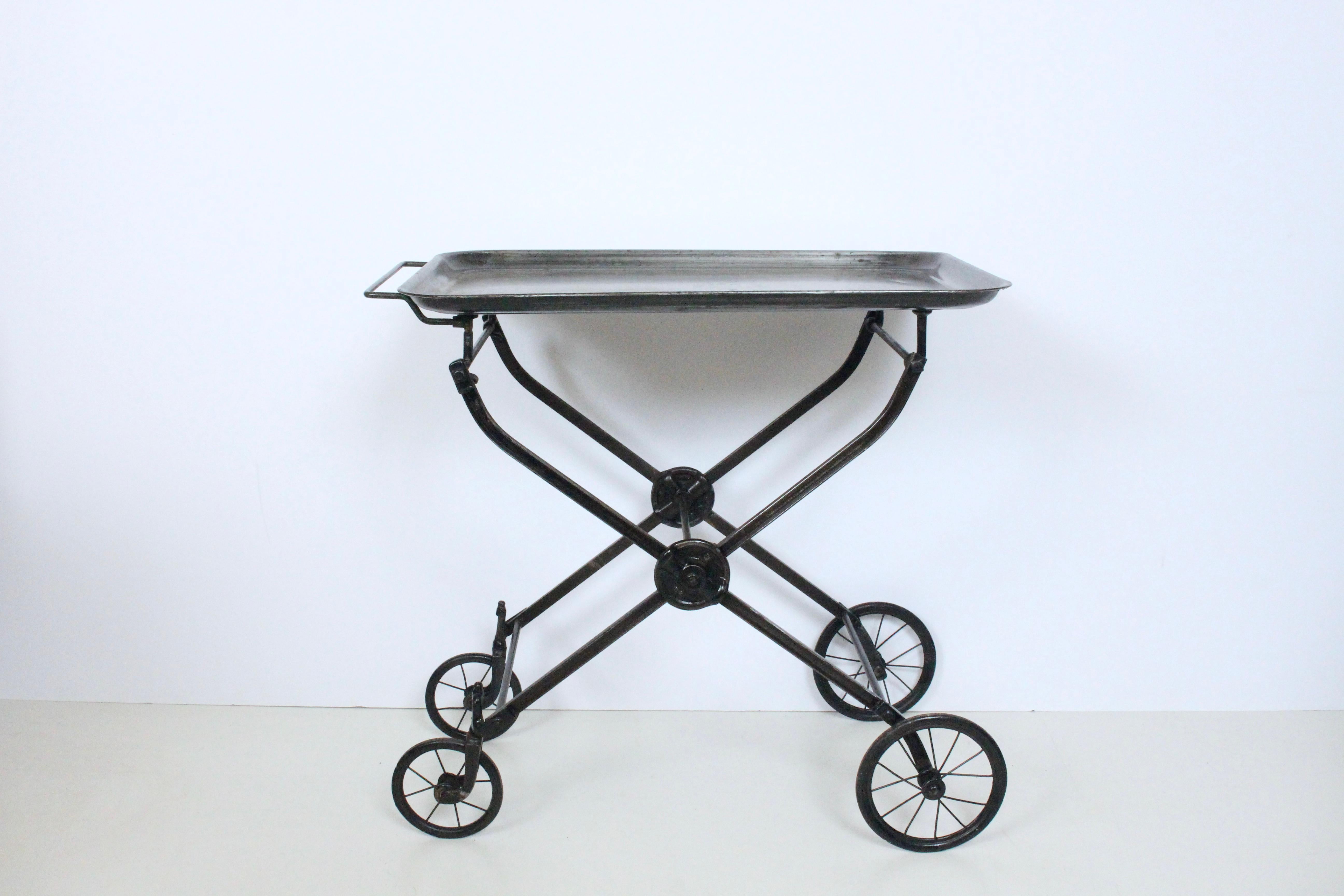 Handled rolling and folding iron hotel beverage trolley, serving cart, dry bar. Tea. Coffee. Plants. Display. Featuring a rectangular larger lipped tray, sturdy Iron crossbar and castings with spoked wheel detail. Uncommon. Industrial. Fine design. 