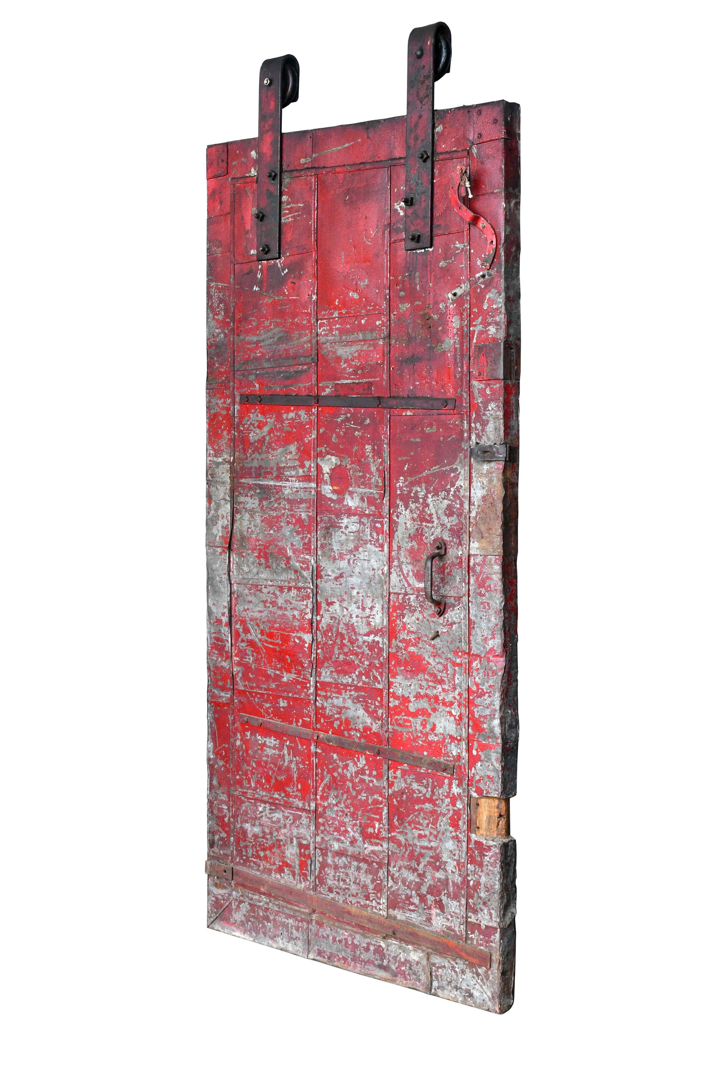 Heavy duty rolling steel fire door manufactured by Syracuse Fire Door Company. The red paint is worn off in places, revealing the metal underneath. Perfect for use as an industrial style barn door, it’s sure to grab attention wherever you put