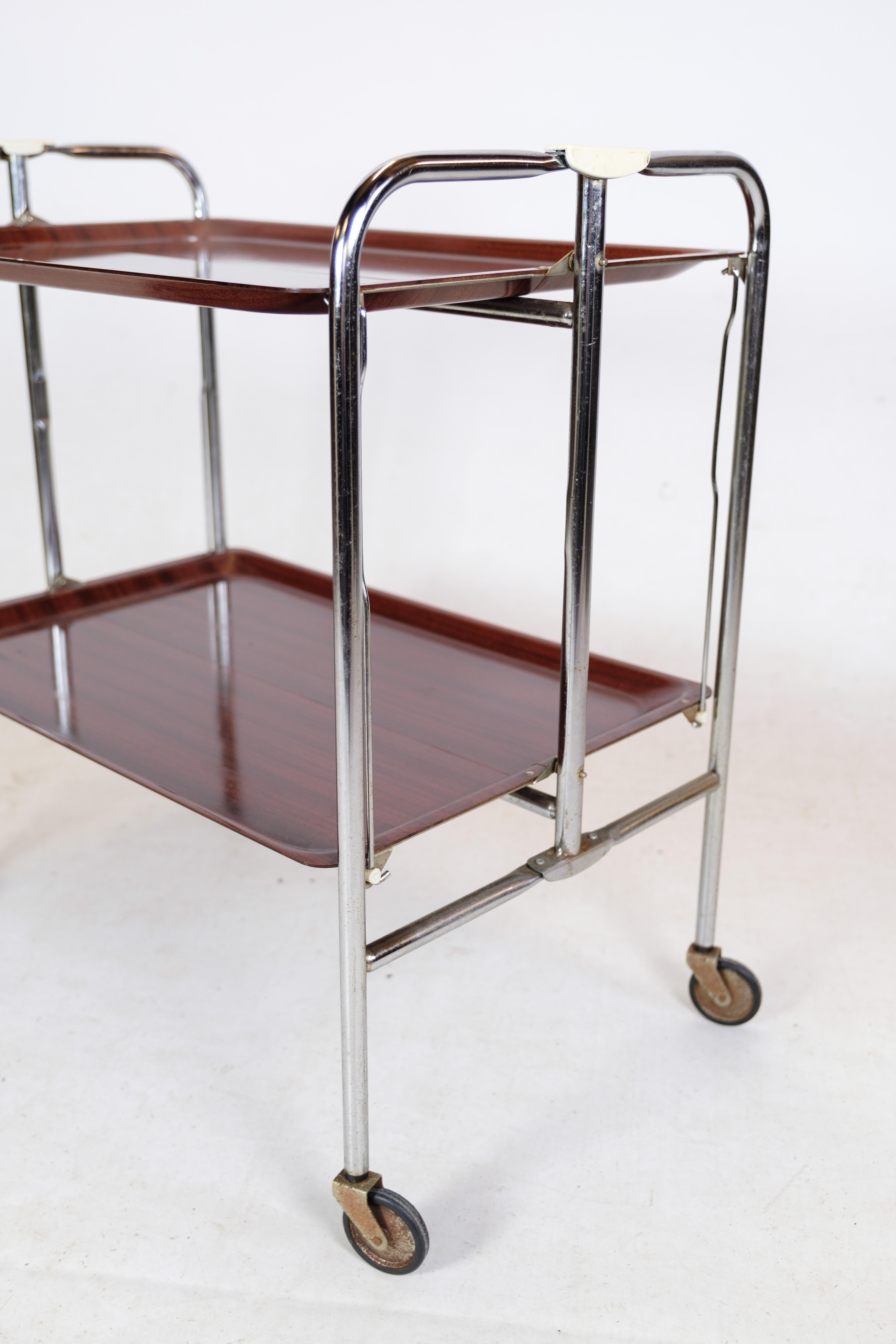 Rollbarer Tisch mit Mahogni-Imitat-Oberfläche, verchromtem Metallgestell und Originalrollen.
Maße in cm: H:68 B:66 T:41