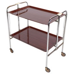 Mesa rodante cromada con superficie de imitación de caoba con ruedas.