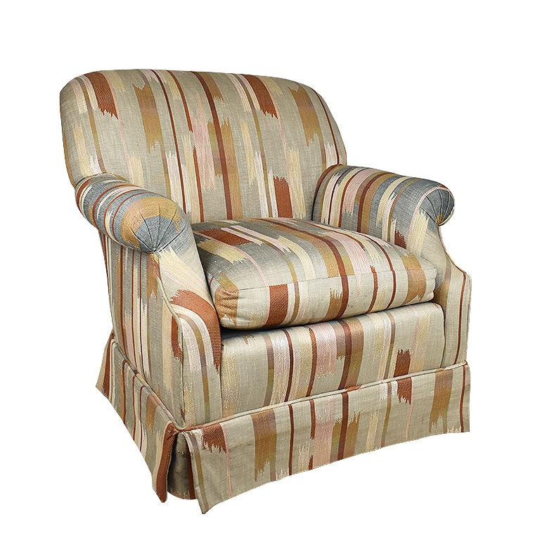 A beautifully upholstered armchair by Baker Furniture Company. This Classic Baker chair is upholstered in a thick ikat or southwest print in orange, blue, yellow, and cream. It has rolled arms and a matching skirt. Wheels at the bottom make it easy