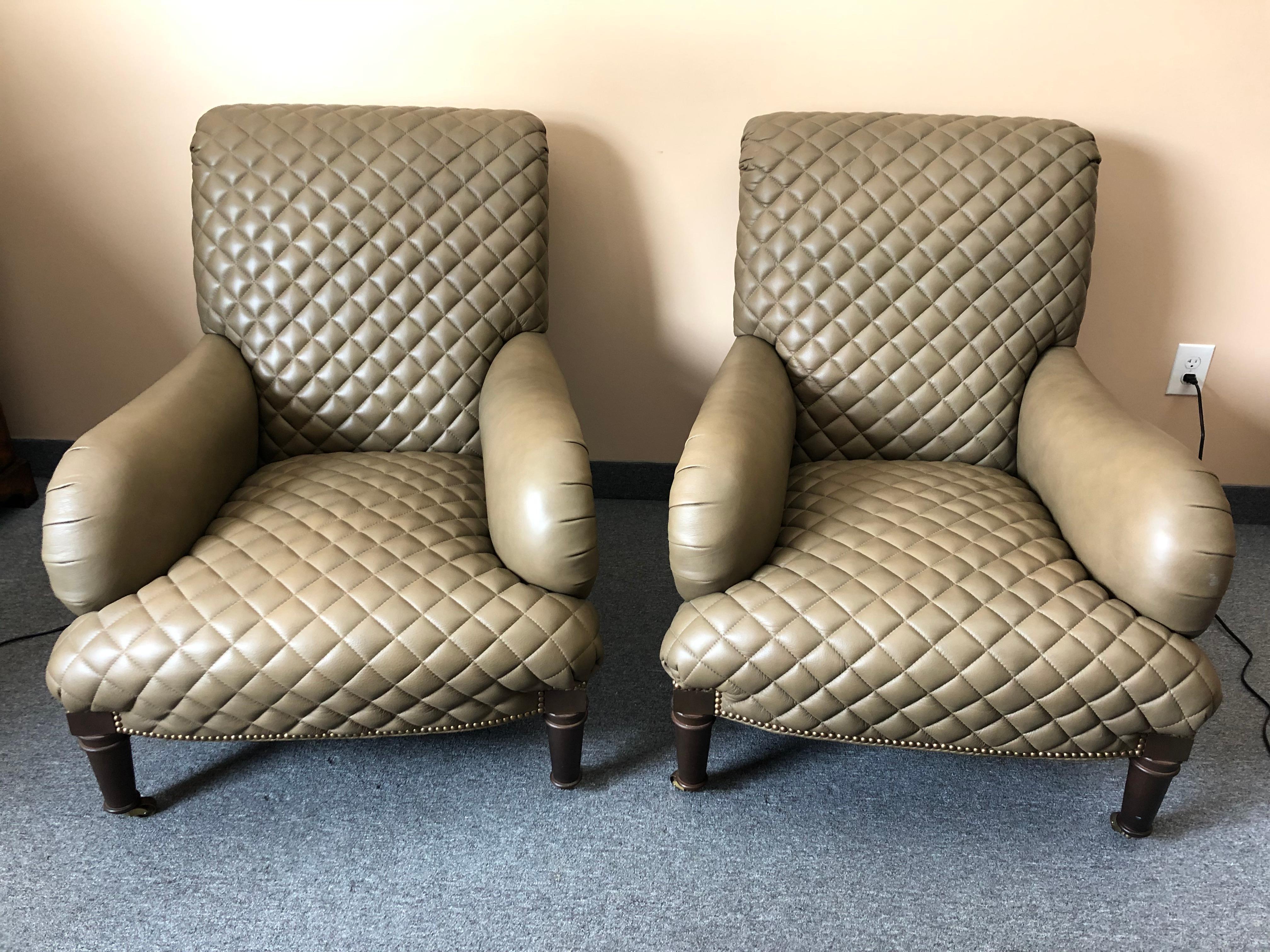Sumptuous pair of taupe quilted leather club chairs and ottomans having gorgeous workmanship, nailhead detailing, and mahogany turned feet on casters. The ottomans curve to fit into the chairs to allow them to be used like chaises. 
Measures: Chair