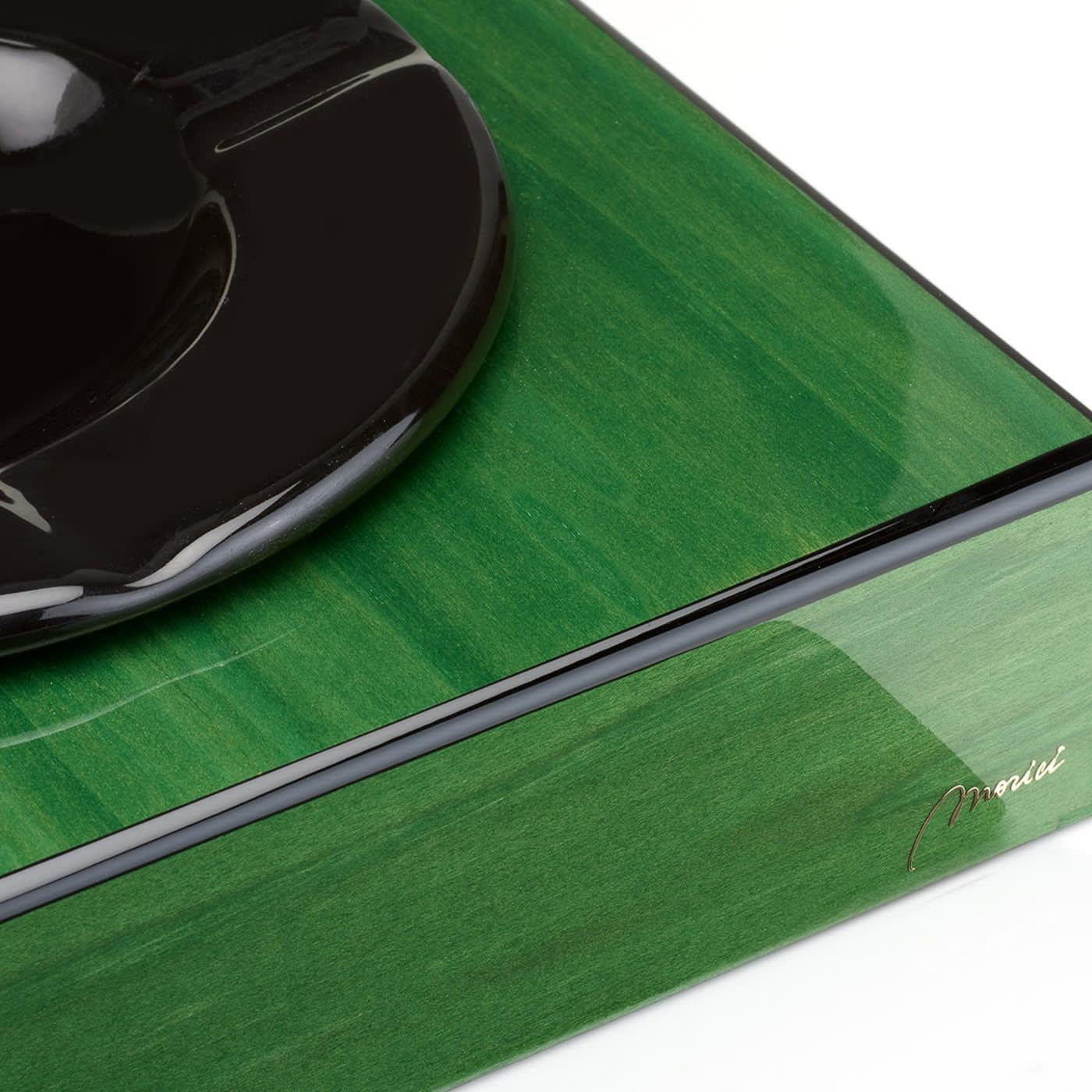 Dieser Aschenbecher, dessen natürliche Maserung durch die polierte grüne und schwarze Farbe hervorgehoben wird, die die klare und klassische Form ziert, verwandelt einen Alltagsgegenstand in ein raffiniertes Stück Inneneinrichtung. Er ist aus Holz