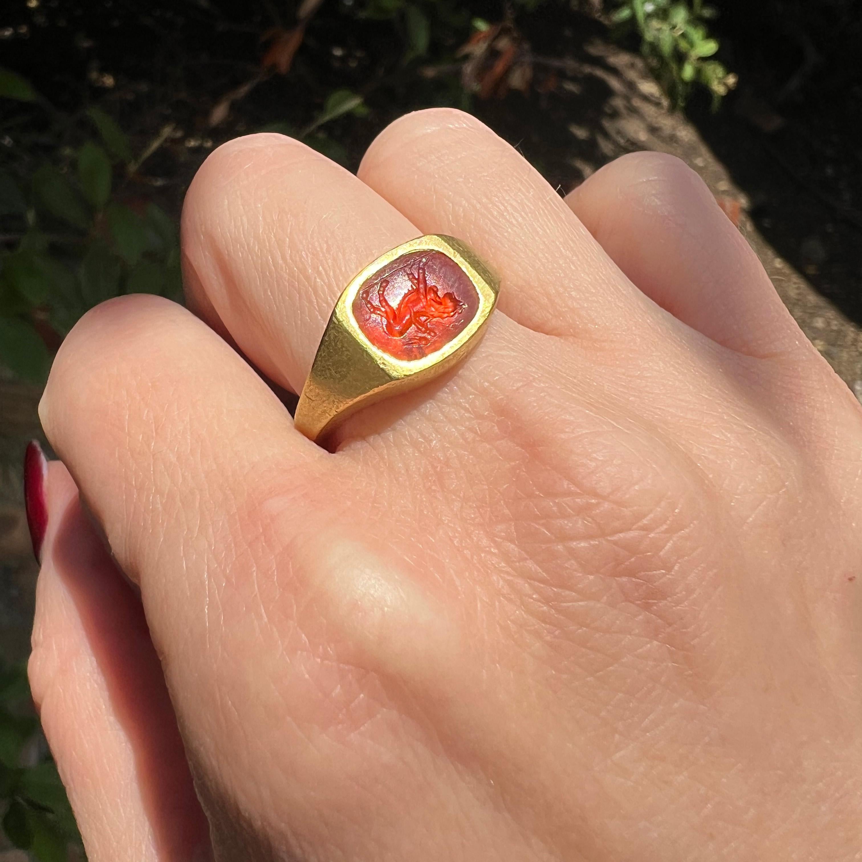 This antique signet ring features a Roman carnelian intaglio depicting Cupid riding a lion. The intaglio is set in a 22kt gold shank, and the shank of the ring dates to the 19th century,. The detailed carving on the carnelian showcases the fine