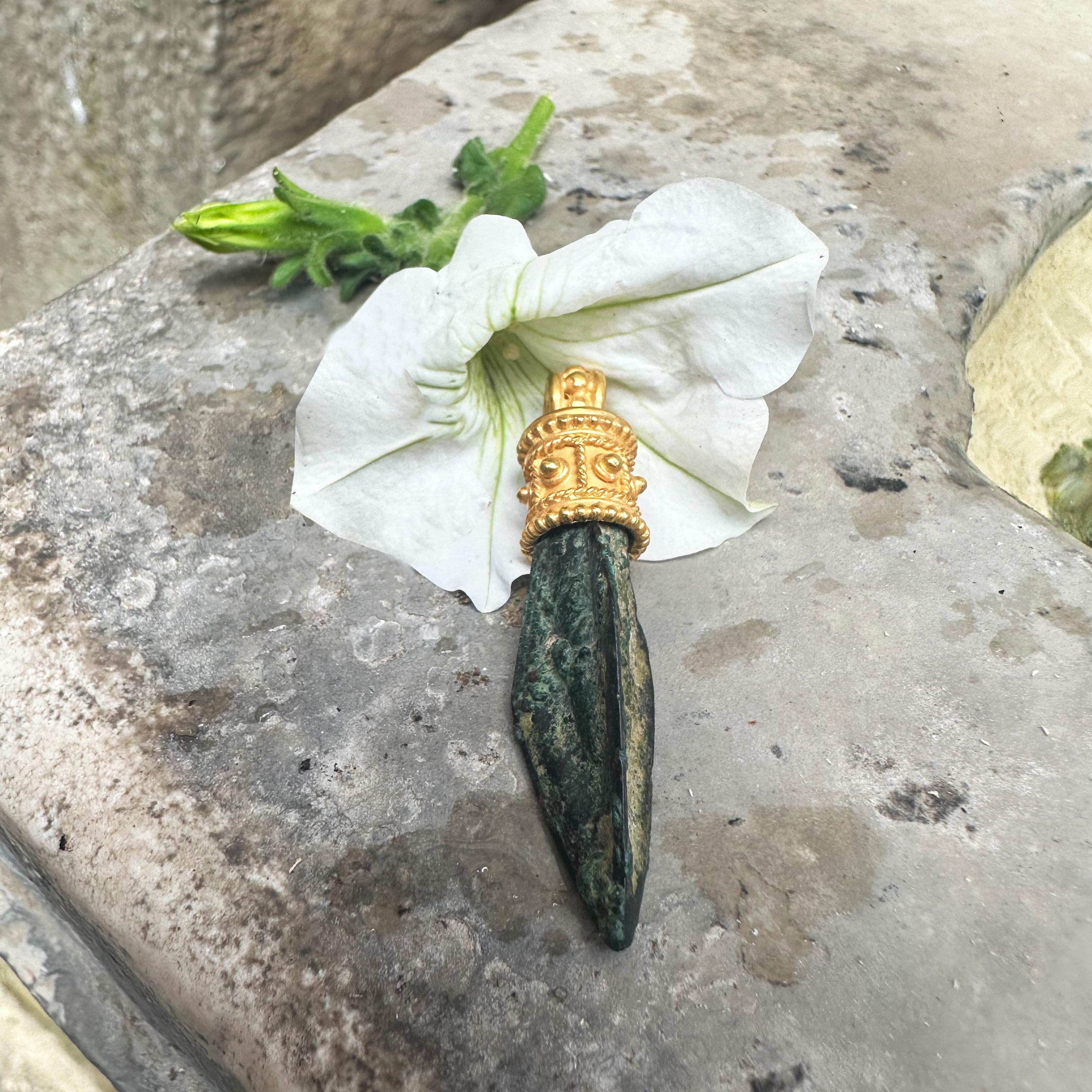 Esta pequeña punta de flecha de bronce, que presenta una pátina verde oliva, se parece a los ejemplos de la Colección Villa Julia. Está montado en oro de 18 quilates y luce un diseño exclusivo de la tienda Serra. La forma más común de punta de