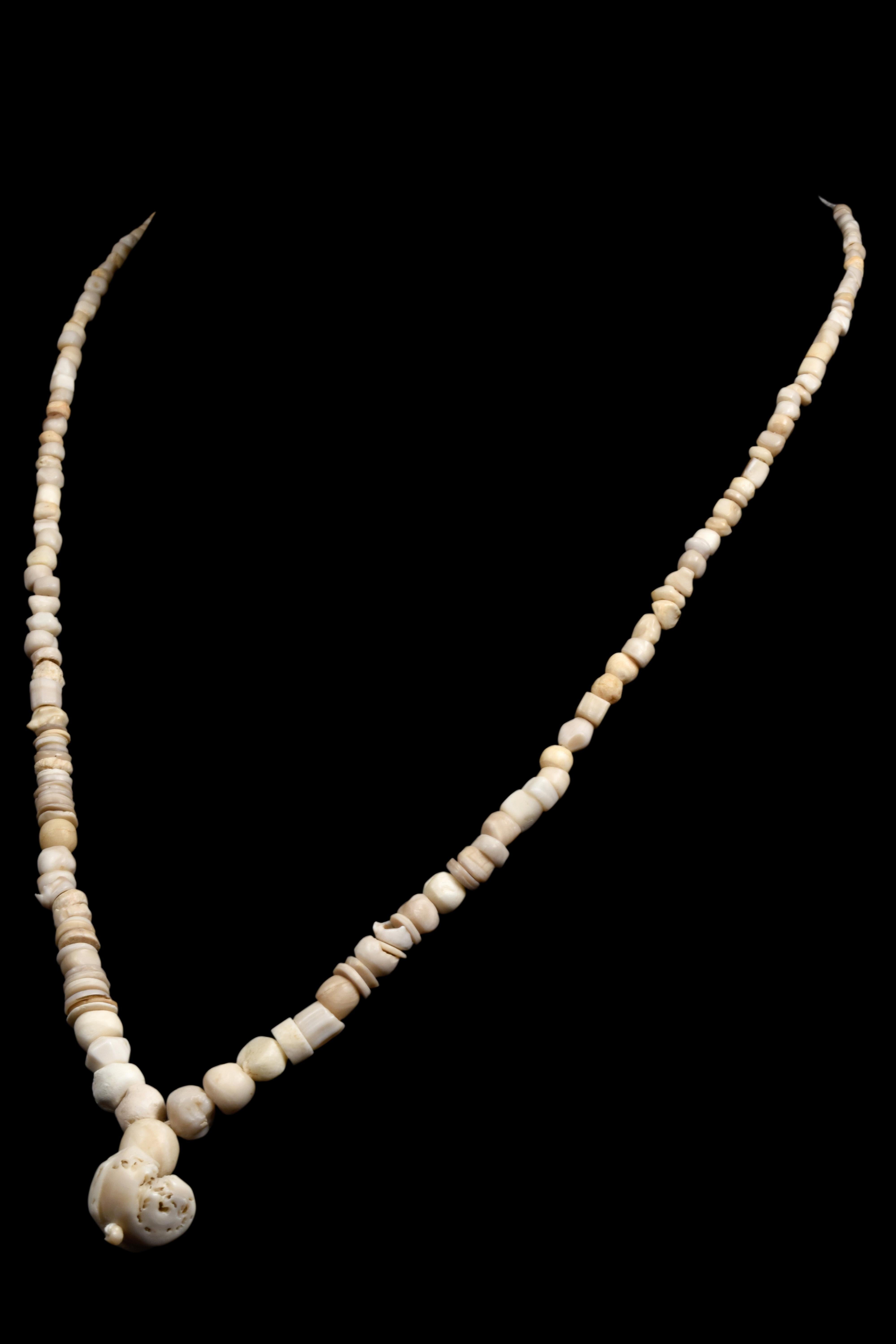 A restrung Roman stone necklace with cream and beige beads, featuring a central pendant comprised of a large, perforated stone. Roman stone beads varied in material and were valued for decoration and status.

Size: L: 220/440mm / W: 5mm ;