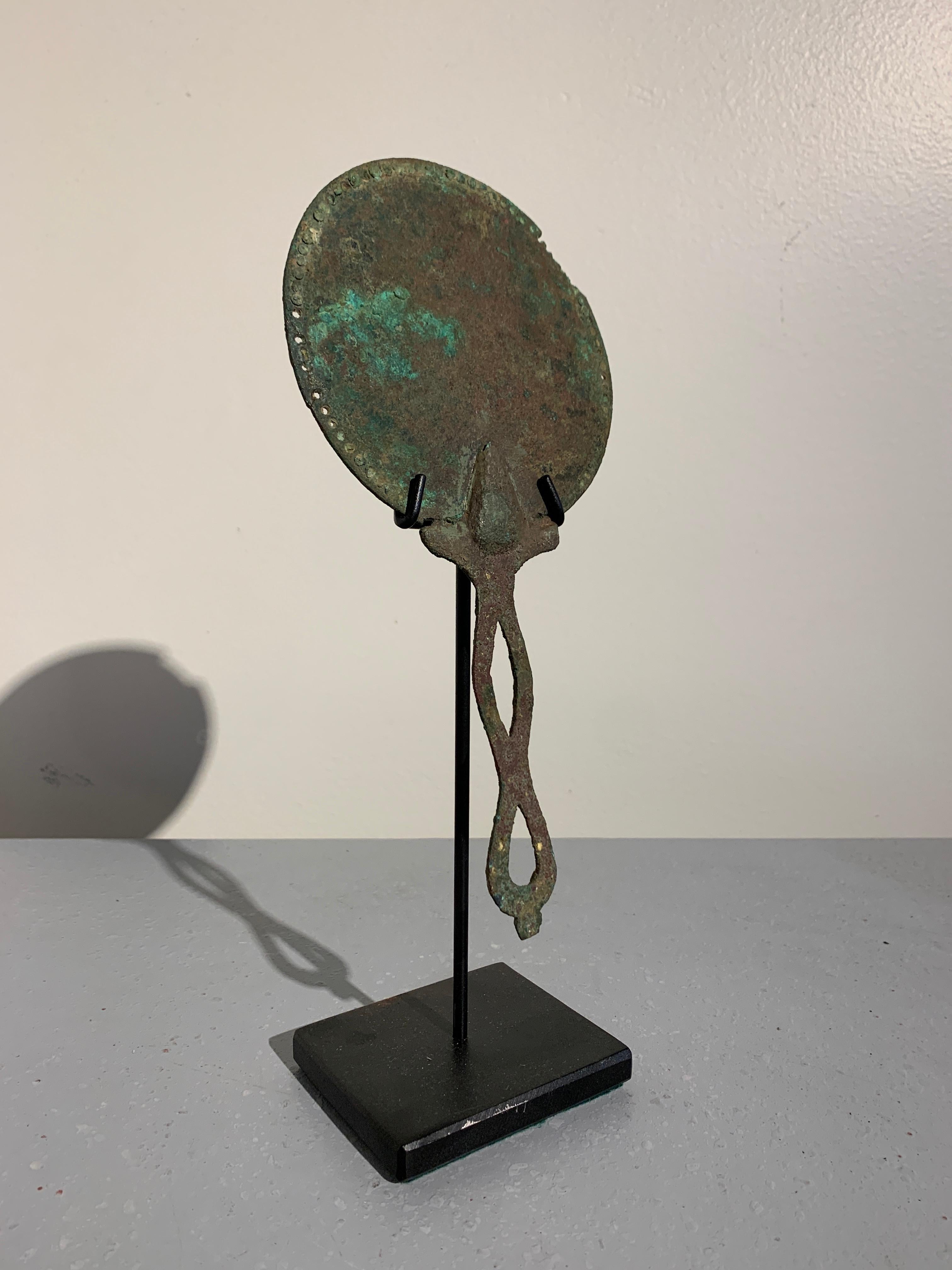 A simple and elegant Roman bronze hand mirror, late Republic Period, circa 1st century, Italy.

The bronze mirror of simple form. The round face with a pierced border design. The openwork handle of twisted form, lending an air of elegance to the