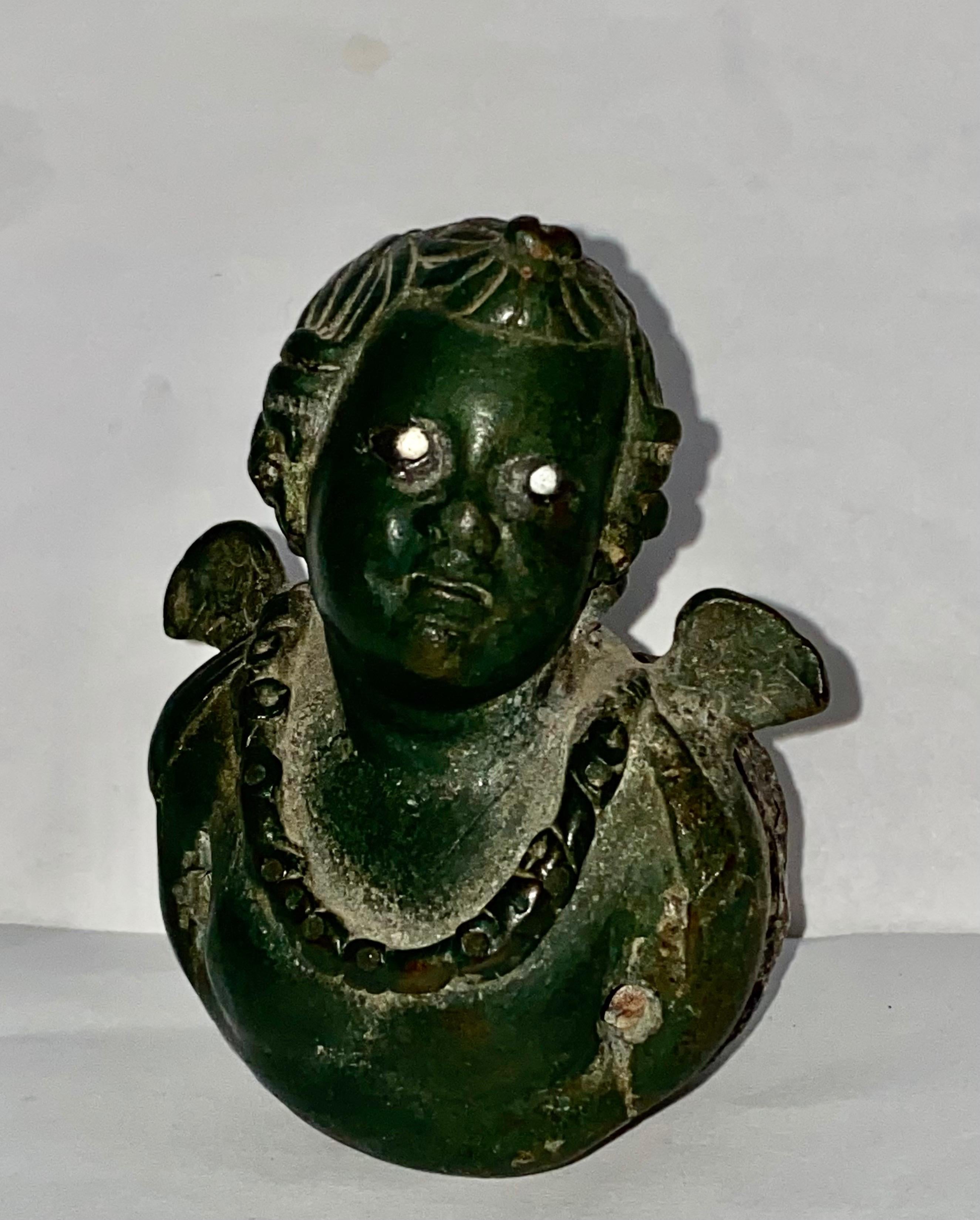 Rome, Imperial Period, ca. 1st century CE. An elegant bronze and lead steelyard weight depicting a Cherub with wings, shown wearing a chain around his neck and with white eyes. with his wavy hair fantastically styled into twists that wraps around