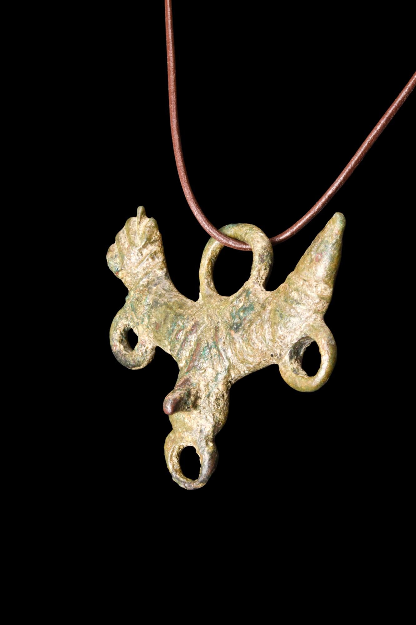 Un ciondolo fallico romano in bronzo che presenta una raffigurazione centrale di un fallo, accompagnato da testicoli intricati. A sinistra c'è una mano alzata in un gesto di manus fica. Il fallo eretto è una rappresentazione visiva della virilità e
