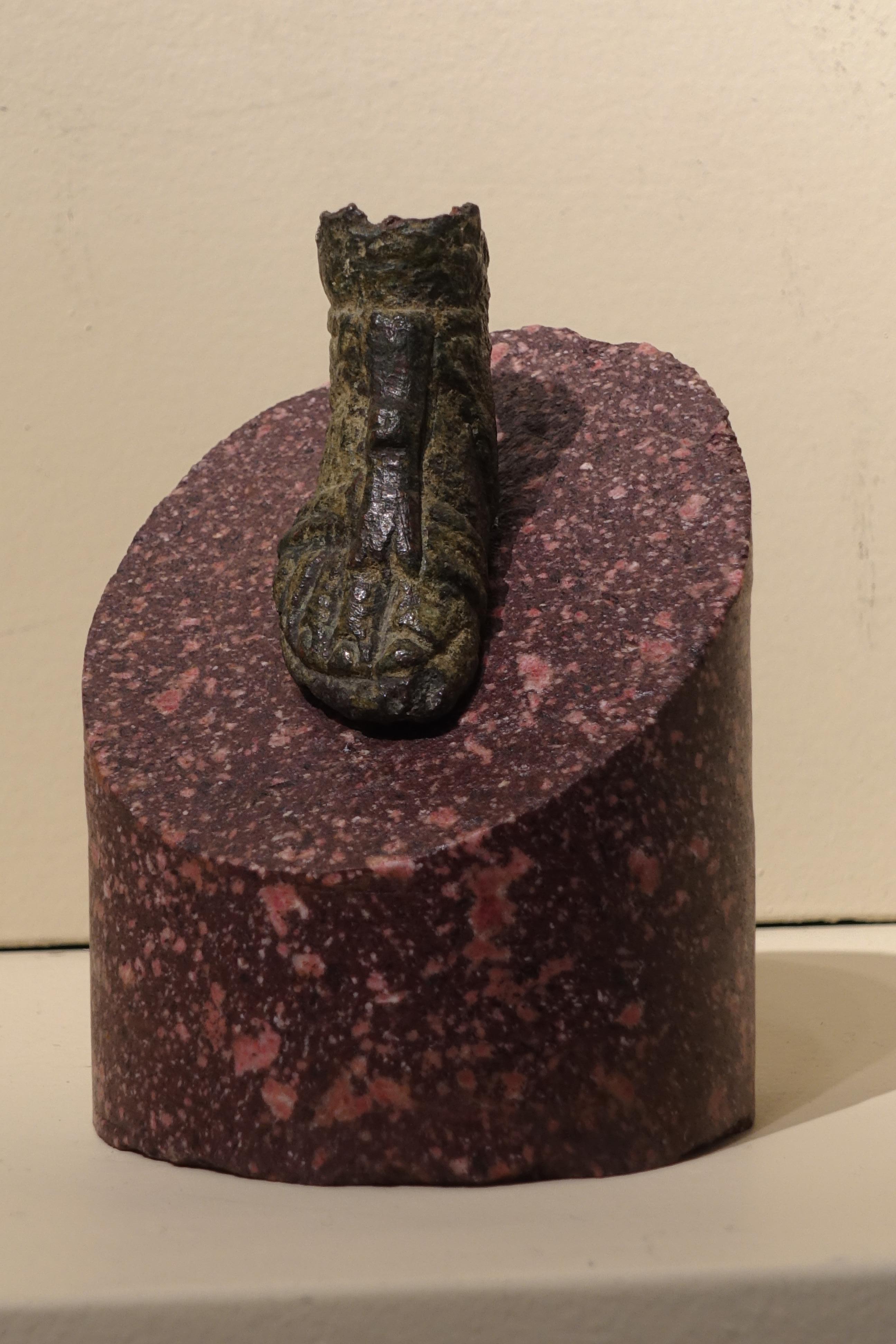 Roman bronze sandaled foot from a statuette
Roman, 2nd century AD
Bronze, on an Egyptian imperial red porphyry base
Foot : Height 3,6 x length 6,3 x depth 2,2 cm
porphyry base : height 8 ; diameter 7 cm

The bronze is enhanced by its rich green