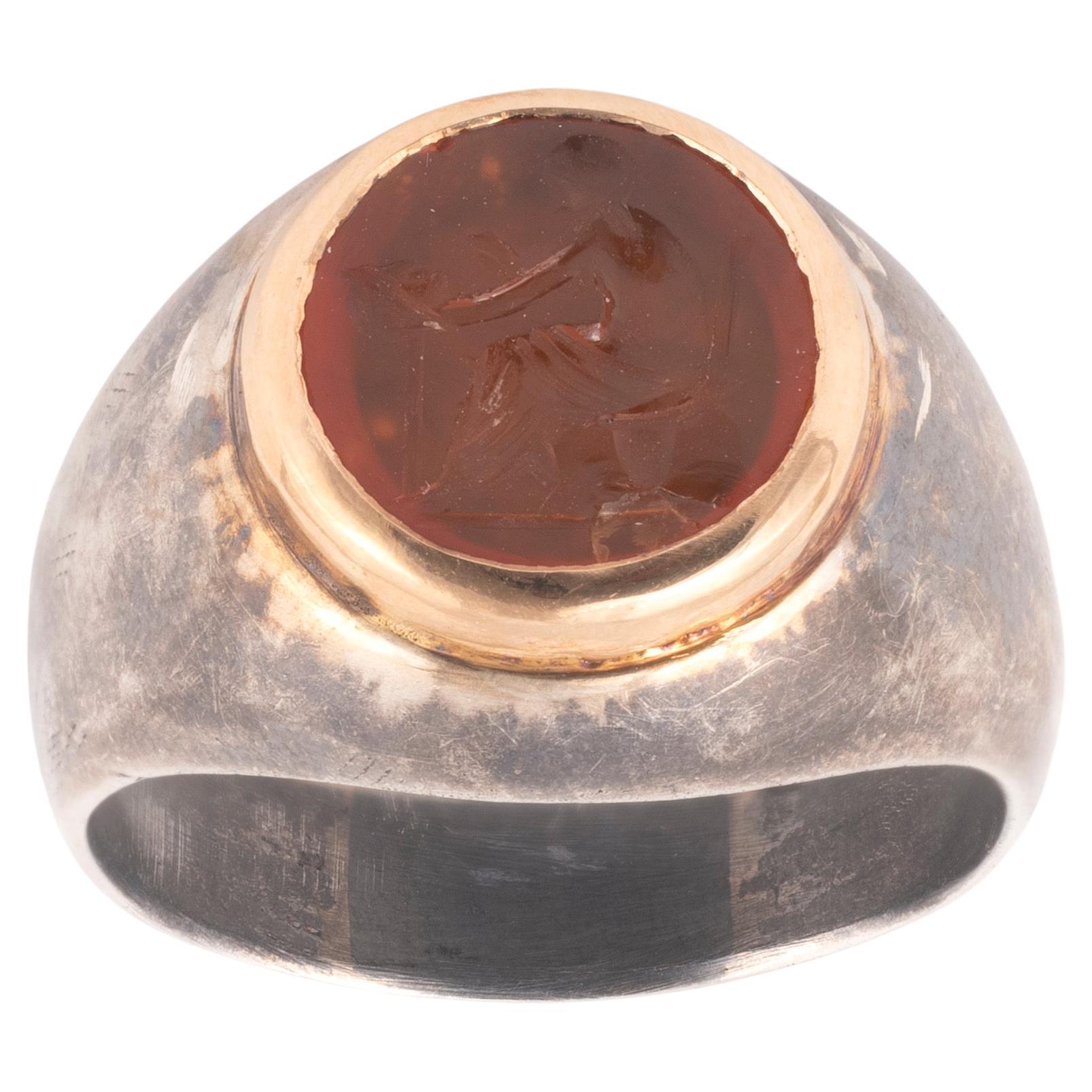 Intaglio rotondo in corniola arancione raffigurante un uomo seduto che tiene una maschera (probabilmente un attore).
Arte romana, II-III secolo. 

Dimensione superiore 12 mm

Anello in argento annerito e oro giallo 18kt
Peso: 13,4